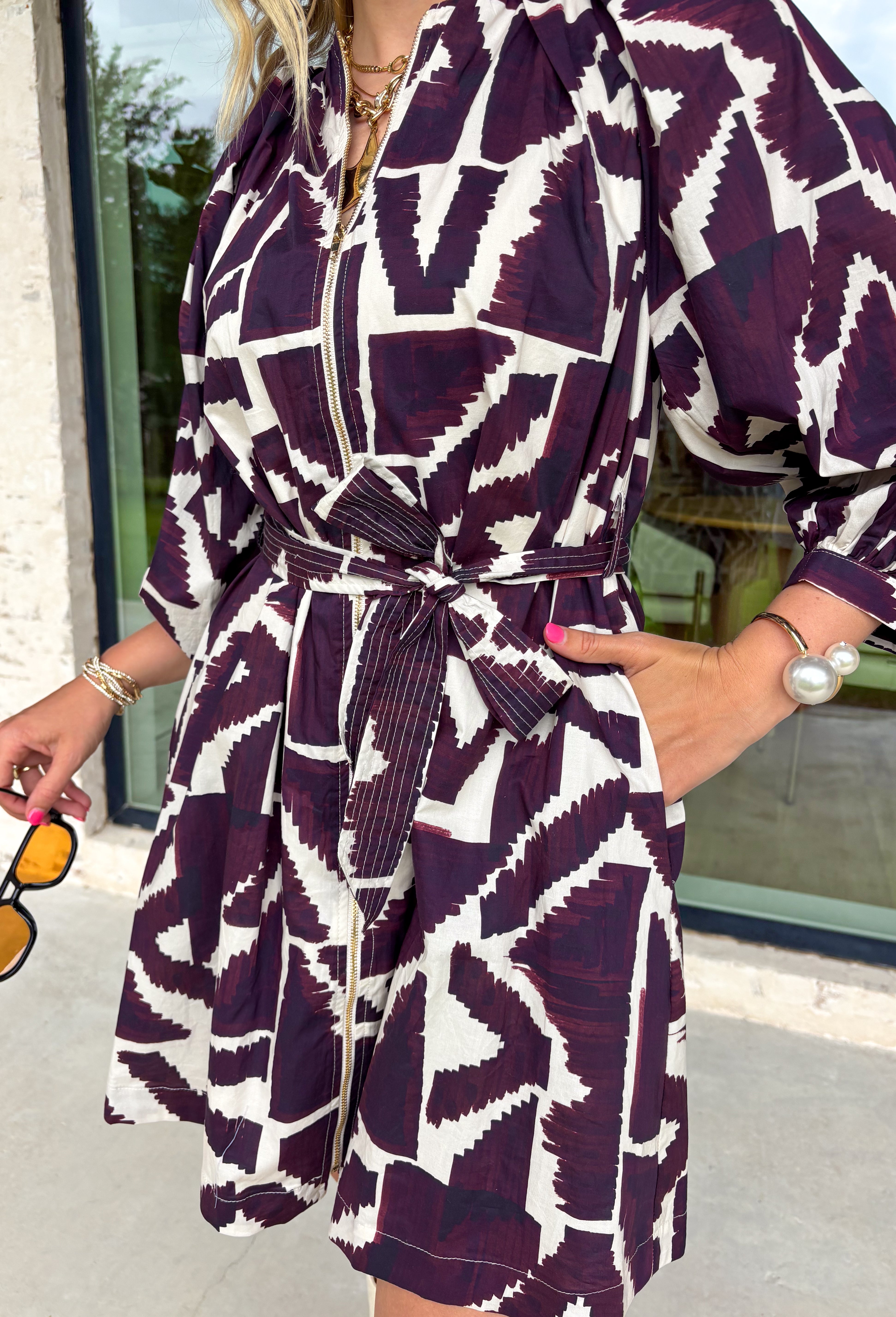 Make a bold yet feminine statement in this merlot and off-white geometric print mini dress by Entro. Designed with ¾ sleeves and a flattering self-tie waist belt, this dress balances comfort and style perfectly. The front zipper closure adds a modern touch, while the full lining keeps it easy and comfortable to wear. With its eye-catching pattern and rich fall tones, this dress is an effortless choice for any special occasion.