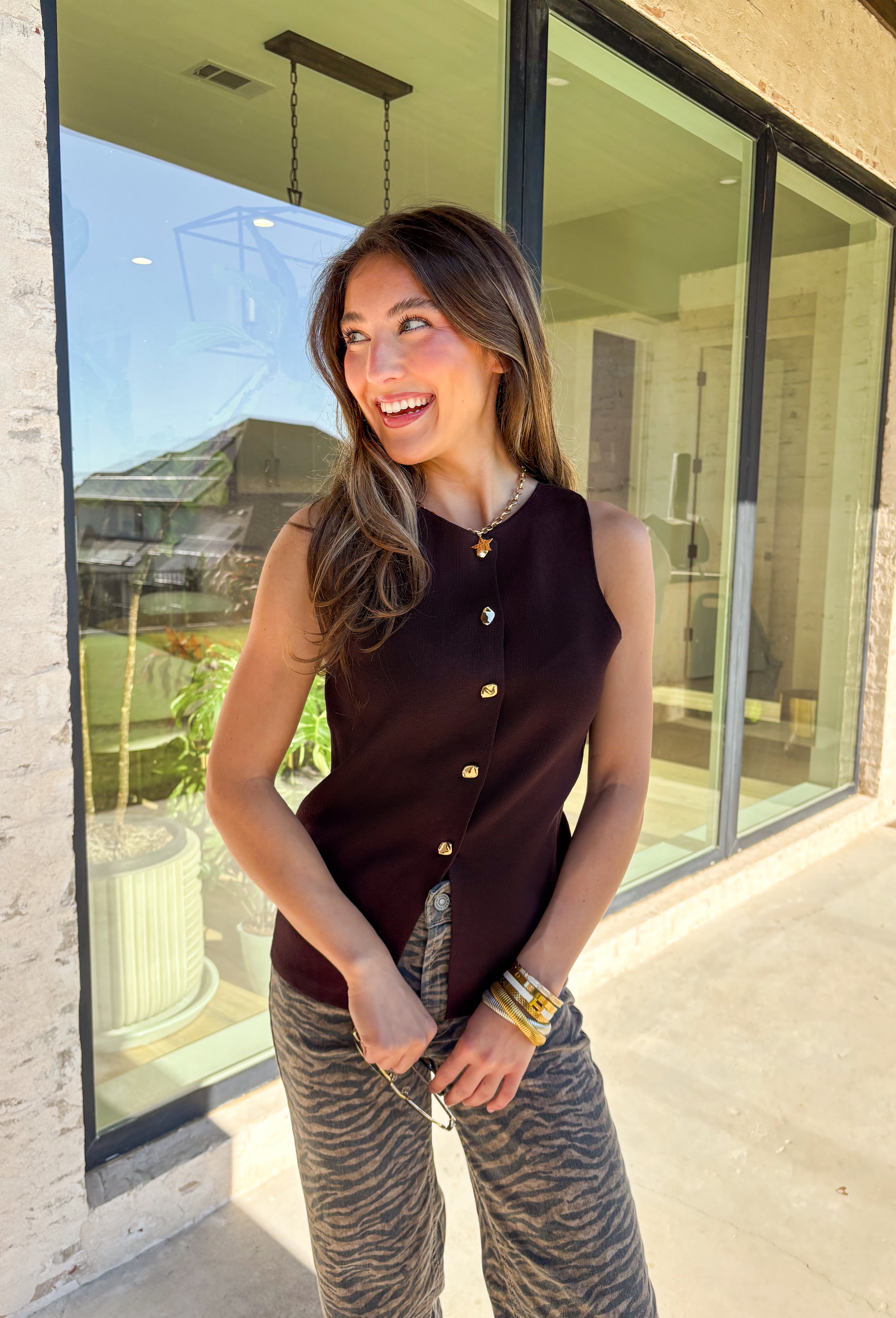 Classic meets modern in this sleeveless brown sweater by Iris. The button-down design is elevated with gold hammered buttons that add a chic, statement touch. Crafted in a soft knit with a lightweight feel, it’s perfect for layering under jackets or wearing solo on warmer days. A versatile piece that easily transitions from casual outings to dressier occasions.