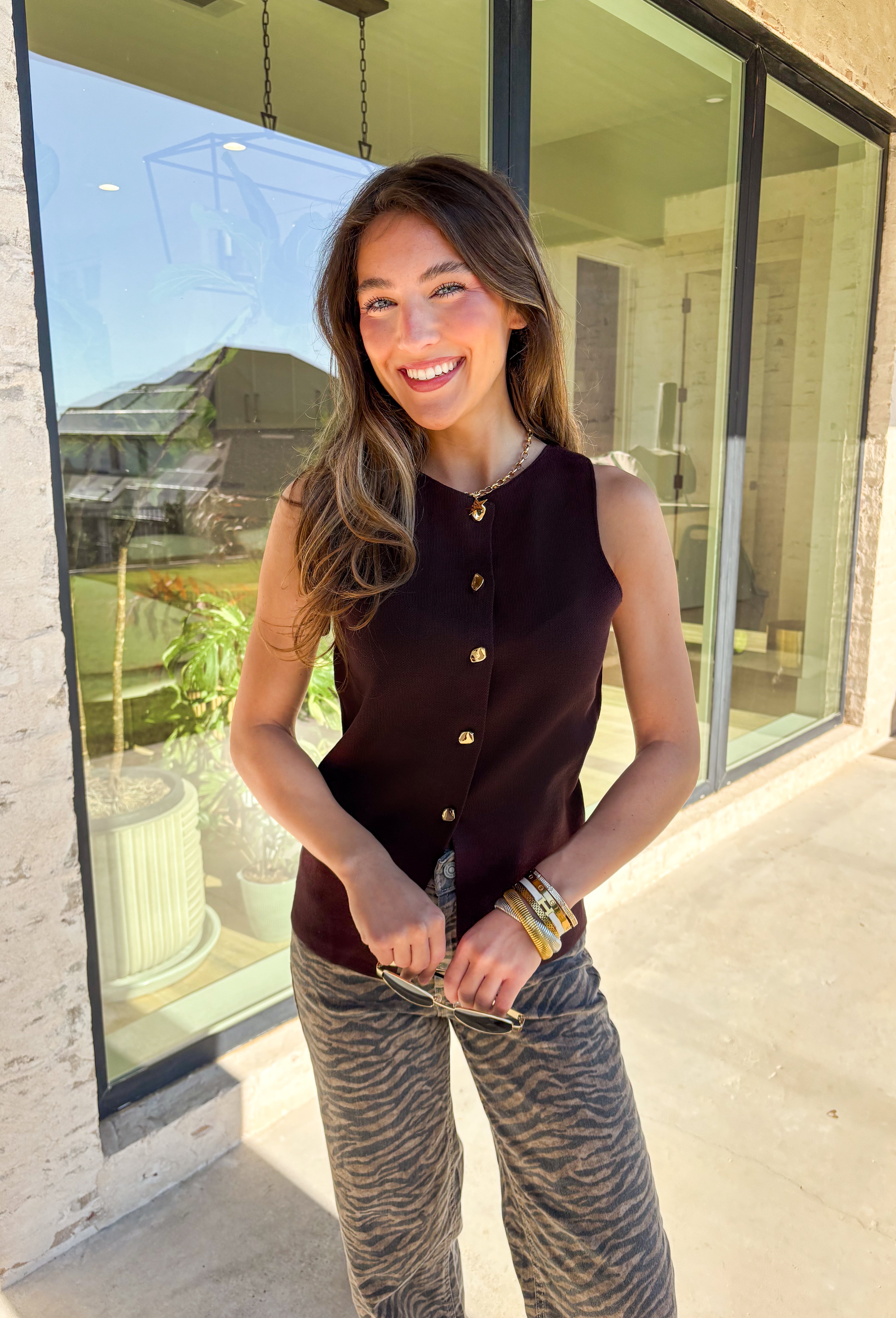 Classic meets modern in this sleeveless brown sweater by Iris. The button-down design is elevated with gold hammered buttons that add a chic, statement touch. Crafted in a soft knit with a lightweight feel, it’s perfect for layering under jackets or wearing solo on warmer days. A versatile piece that easily transitions from casual outings to dressier occasions.