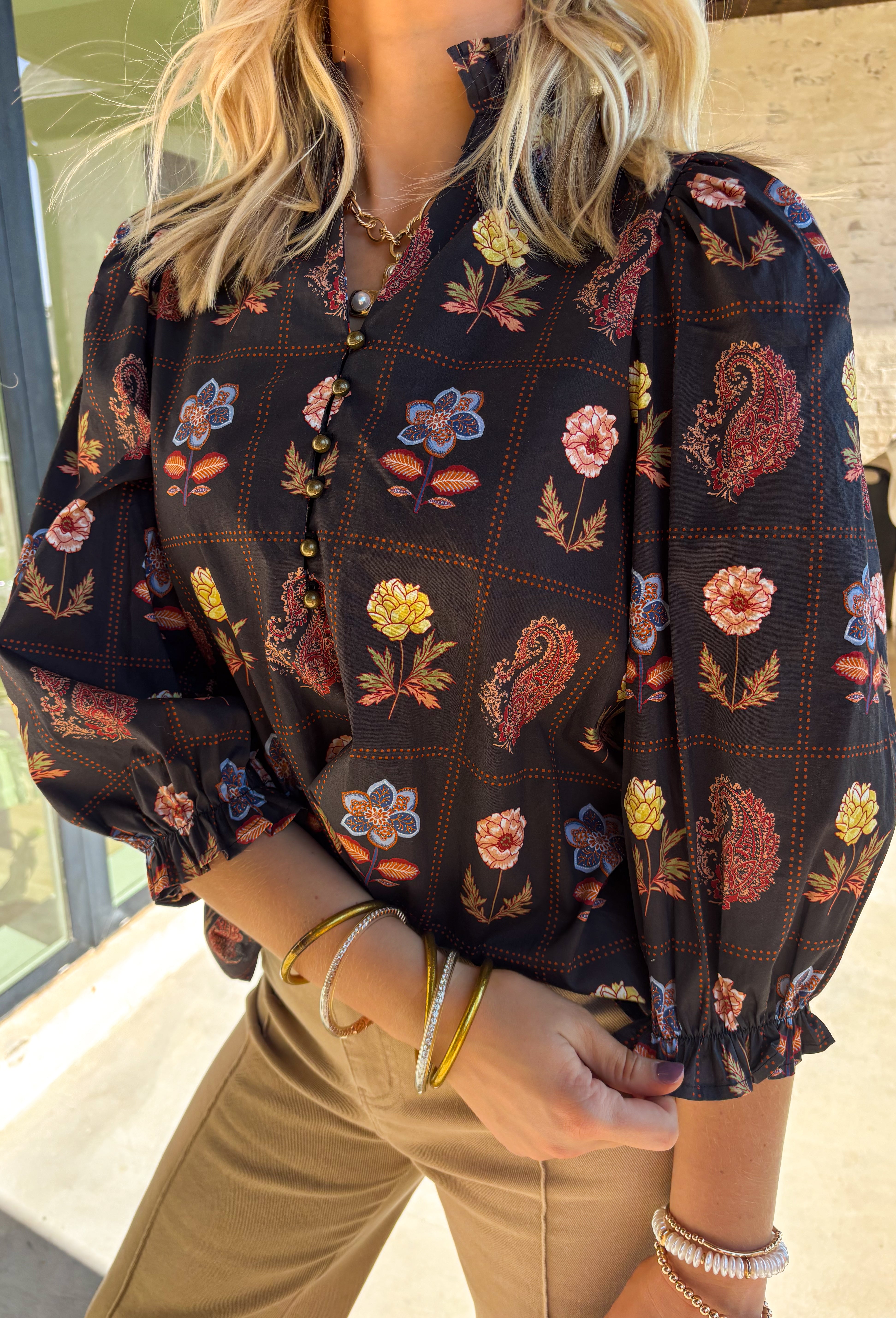A statement piece for the season, this black top by Entro brings together rich autumn tones and timeless details. Featuring a mix of floral and paisley prints, it’s designed with ¾ puff sleeves, a ruffled high neckline, and a delicate loop-button closure at the front. Elasticated sleeve openings with ruffle trim add a feminine finish. Crafted from soft cotton with a hint of stretch, this top is as comfortable as it is stylish—perfect for dressing up or down this fall.