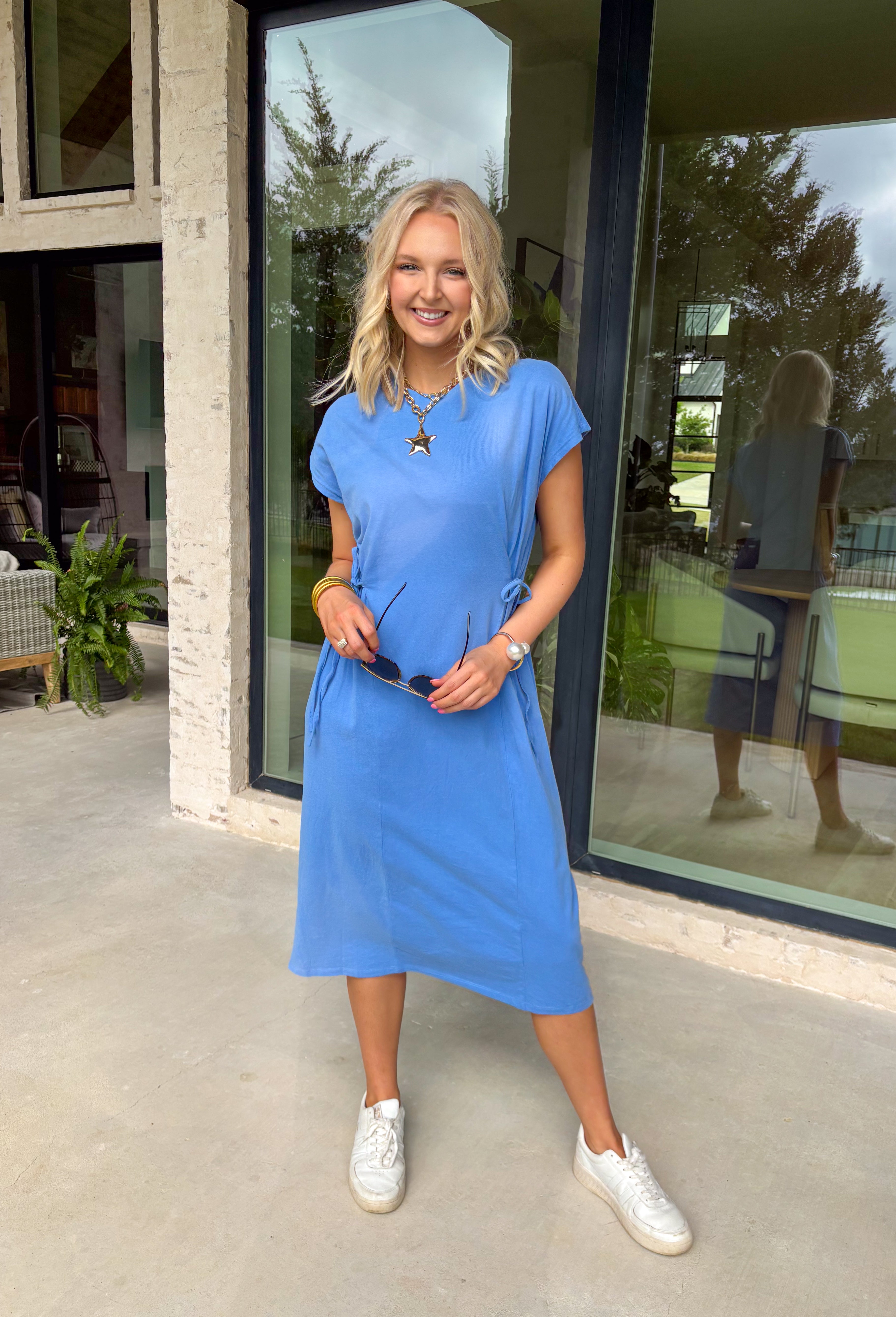 This blue short sleeve midi dress is the kind of effortless piece that makes summer styling so easy! Made from lightweight, breathable cotton, it’s perfect for warm days when you want to feel comfortable but still look put together. The tie details at each hip add a flattering, adjustable touch that gives shape while keeping things relaxed. With its easy midi length and throw-on-and-go feel, this is the dress you’ll reach for on repeat—from casual days to dinner plans. 