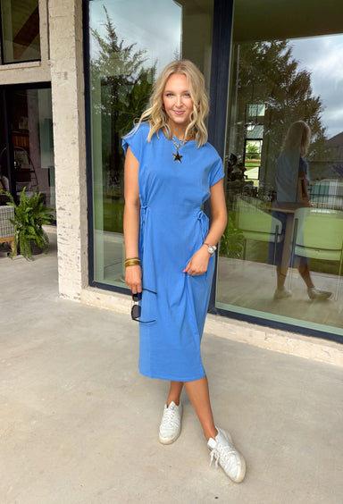 This blue short sleeve midi dress is the kind of effortless piece that makes summer styling so easy! Made from lightweight, breathable cotton, it’s perfect for warm days when you want to feel comfortable but still look put together. The tie details at each hip add a flattering, adjustable touch that gives shape while keeping things relaxed. With its easy midi length and throw-on-and-go feel, this is the dress you’ll reach for on repeat—from casual days to dinner plans. 