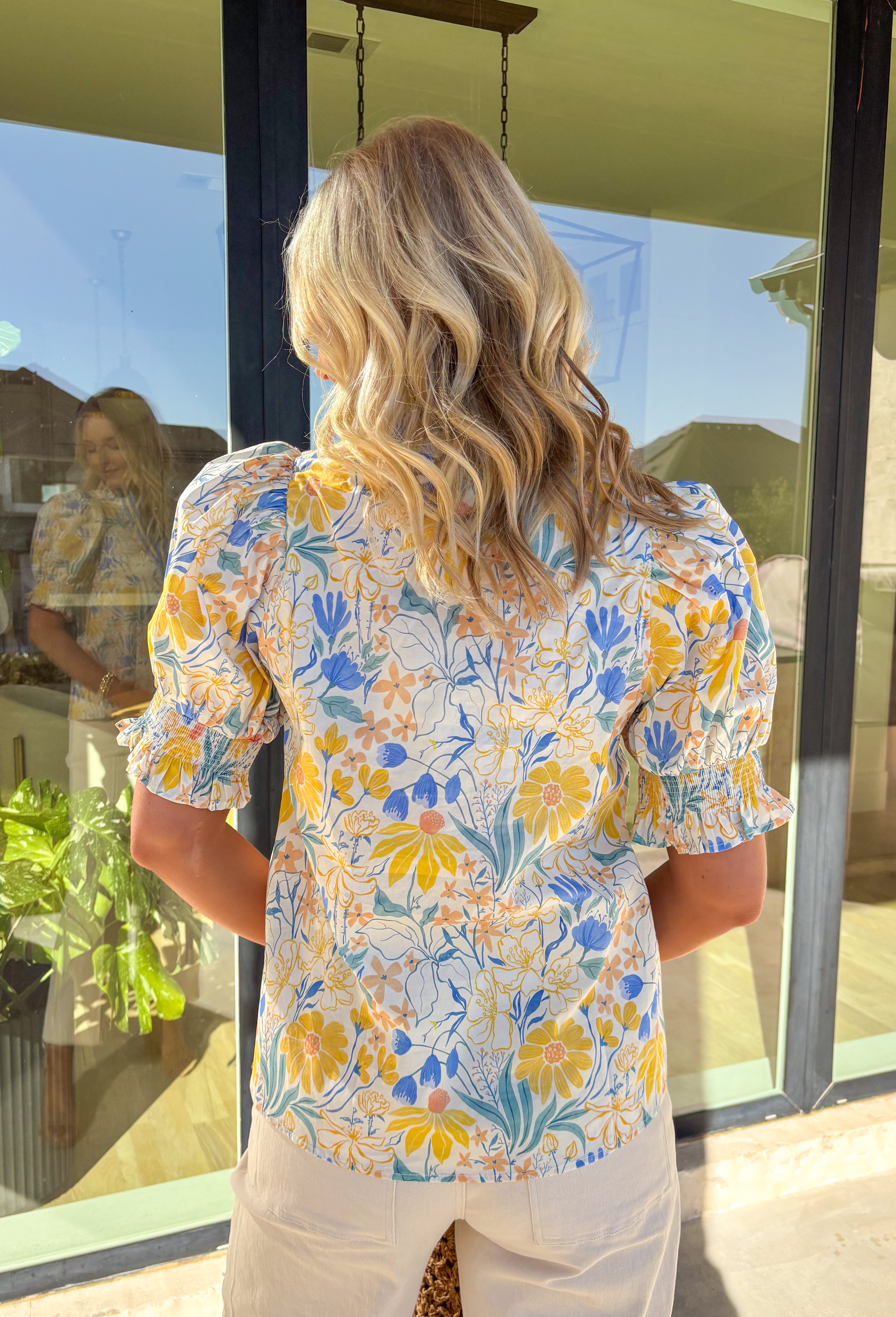 Soft, sunny, and full of spring charm, this off-white short sleeve top by Entro is an easy favorite for the season. Featuring a yellow and blue floral print, it feels bright and cheerful without being overpowering. The coordinating yellow and blue band along the front adds a fun pop of contrast, while the smocked neckline and ruffle sleeves bring a sweet, feminine finish. Crafted from breathable cotton, this top is perfect for warm spring days.