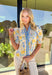 Soft, sunny, and full of spring charm, this off-white short sleeve top by Entro is an easy favorite for the season. Featuring a yellow and blue floral print, it feels bright and cheerful without being overpowering. The coordinating yellow and blue band along the front adds a fun pop of contrast, while the smocked neckline and ruffle sleeves bring a sweet, feminine finish. Crafted from breathable cotton, this top is perfect for warm spring days.