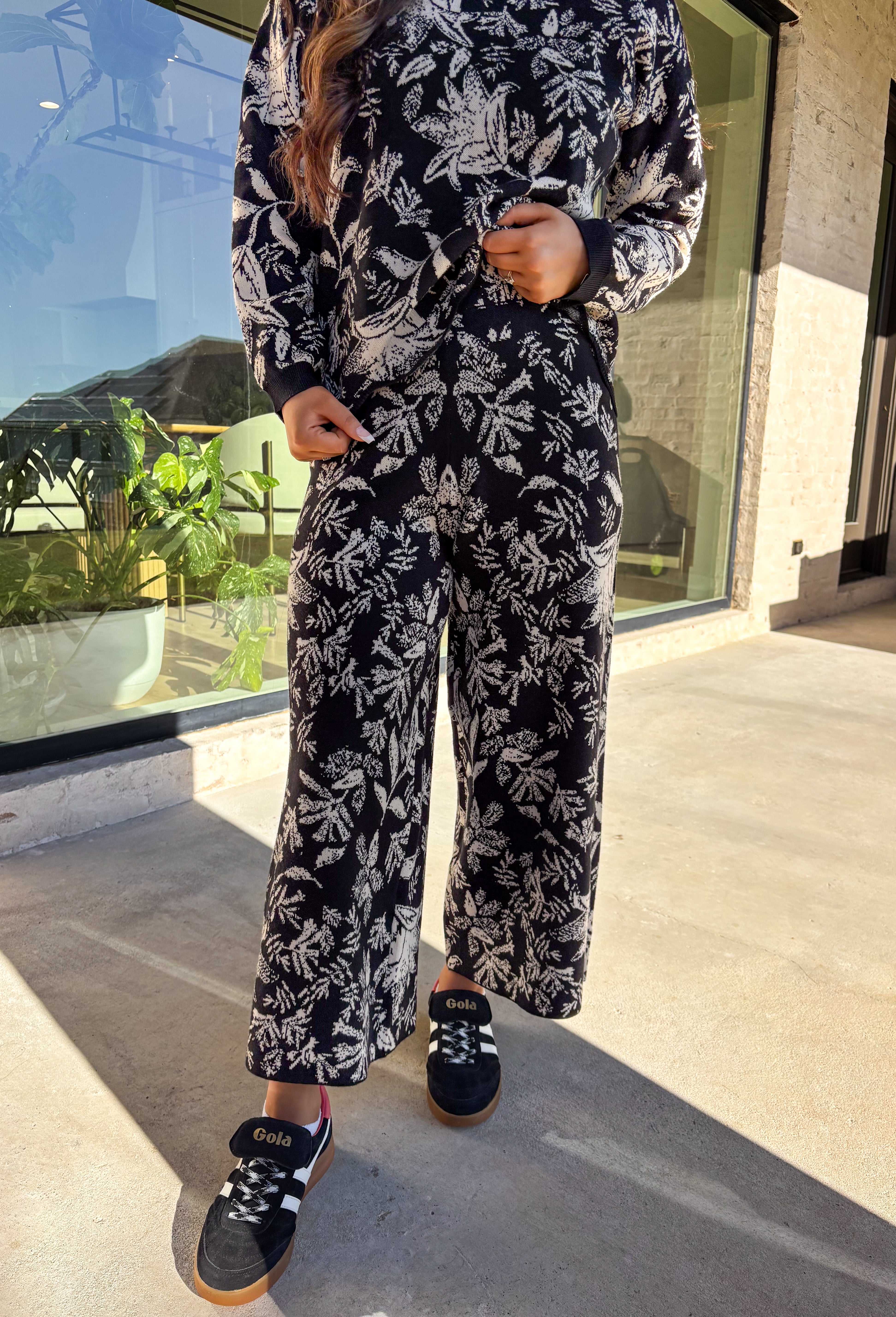 Cozy meets chic in this matching knit set that’s made to turn heads. The black long sleeve top is designed with a cream floral print and finished with a scalloped hem for a sweet touch of detail. Paired with wide leg pants featuring an easy elastic waistband, this set blends lounge-worthy comfort with pulled-together style. Wear the pieces together for a bold coordinated look, or mix and match for endless outfit options.