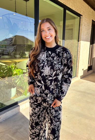 Cozy meets chic in this matching knit set that’s made to turn heads. The black long sleeve top is designed with a cream floral print and finished with a scalloped hem for a sweet touch of detail. Paired with wide leg pants featuring an easy elastic waistband, this set blends lounge-worthy comfort with pulled-together style. Wear the pieces together for a bold coordinated look, or mix and match for endless outfit options.