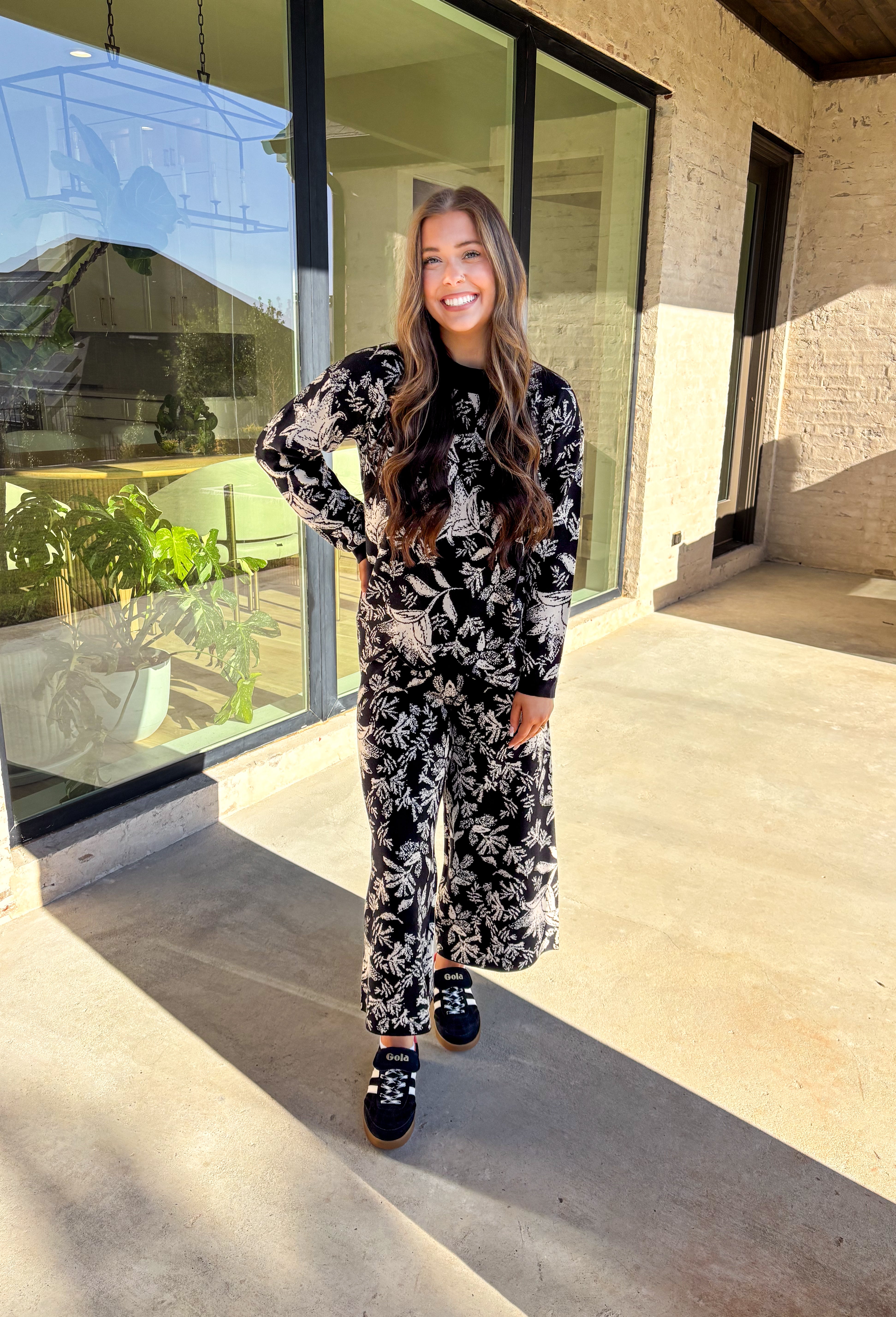 Cozy meets chic in this matching knit set that’s made to turn heads. The black long sleeve top is designed with a cream floral print and finished with a scalloped hem for a sweet touch of detail. Paired with wide leg pants featuring an easy elastic waistband, this set blends lounge-worthy comfort with pulled-together style. Wear the pieces together for a bold coordinated look, or mix and match for endless outfit options.