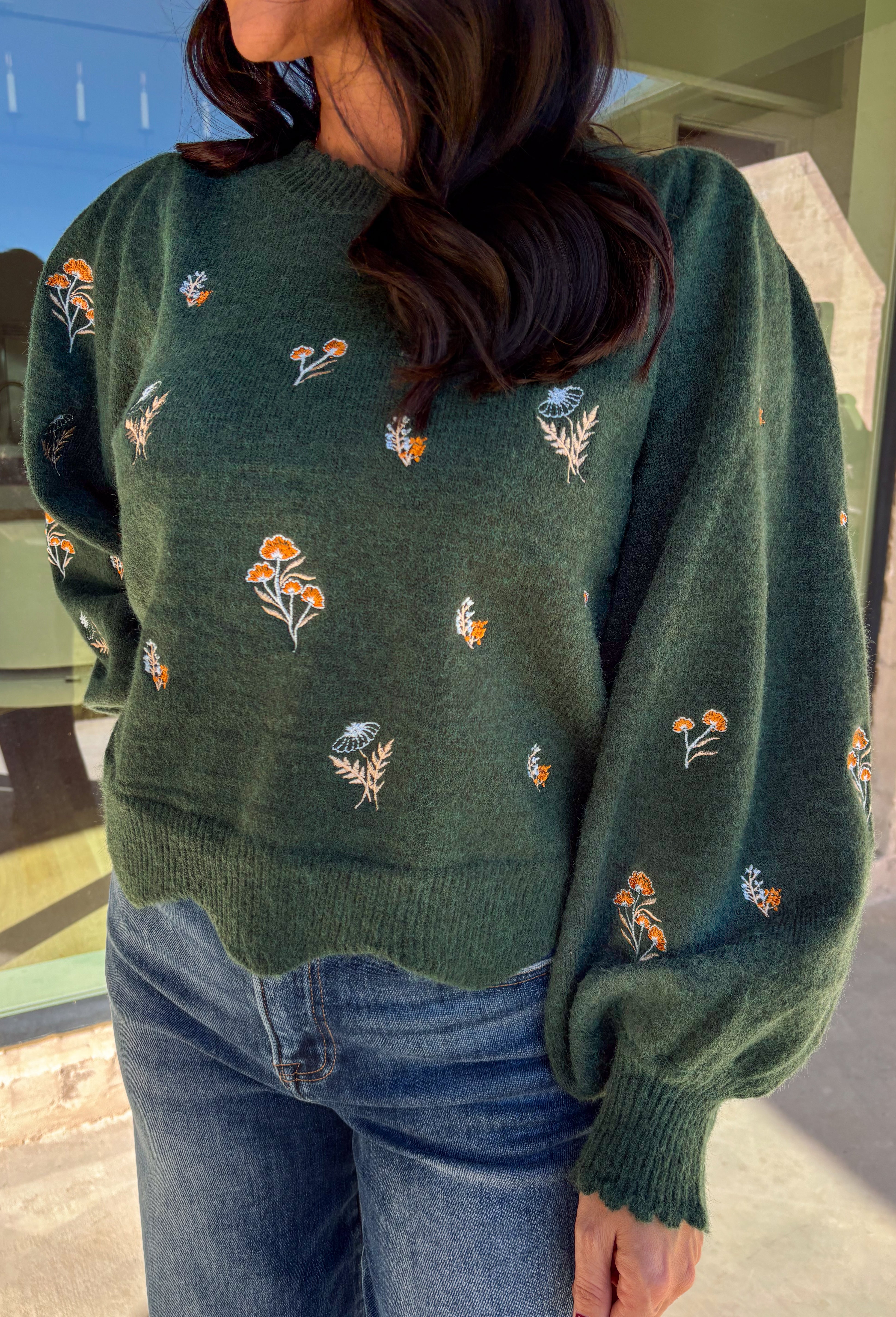 This hunter green sweater by Entro brings cozy charm with a touch of detail. The neutral floral embroidery adds soft texture, while the scalloped neckline and hem give it a sweet, feminine finish. Perfect for cool-weather days, this lightweight knit offers that just-right blend of comfort and style for any fall occasion.