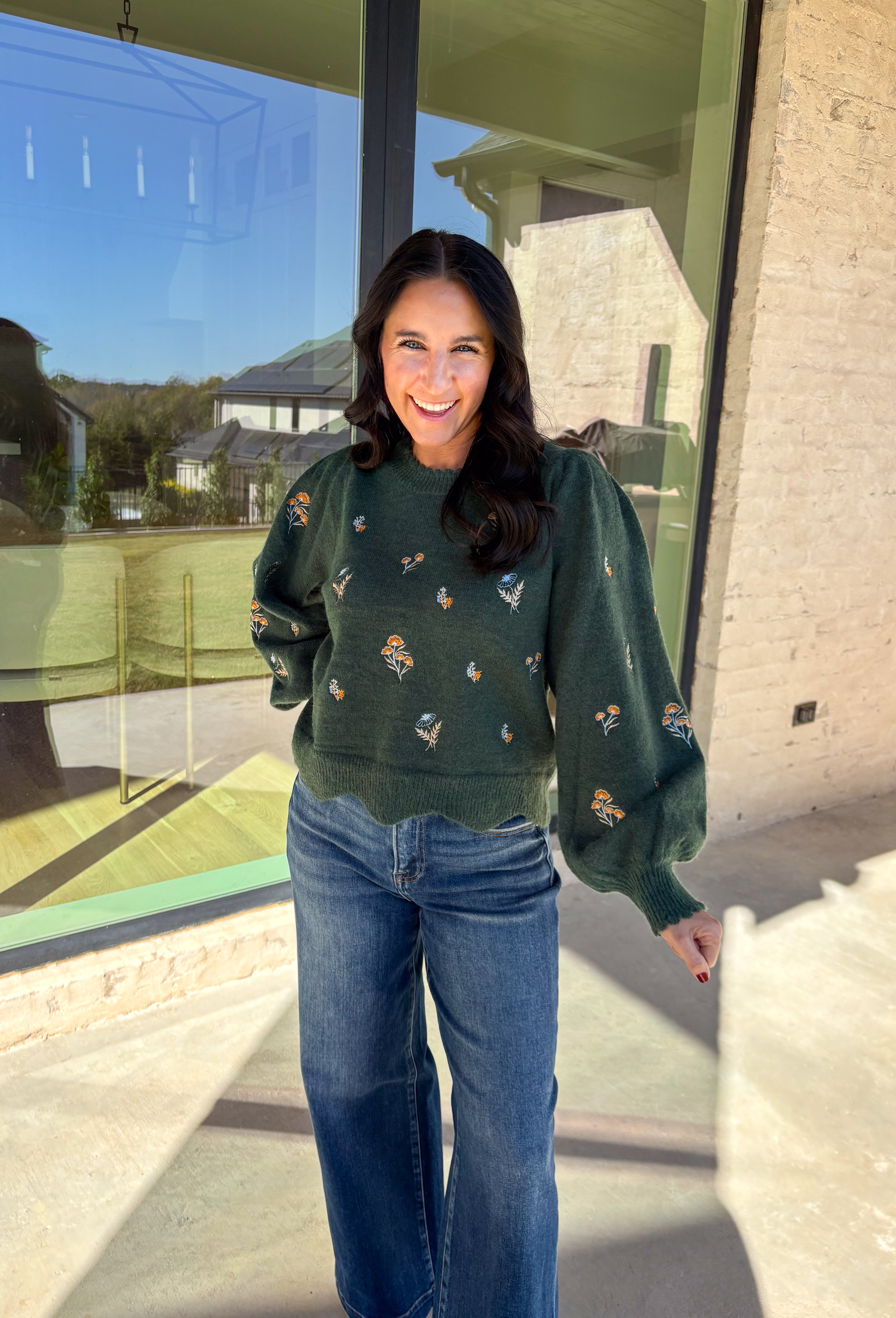 This hunter green sweater by Entro brings cozy charm with a touch of detail. The neutral floral embroidery adds soft texture, while the scalloped neckline and hem give it a sweet, feminine finish. Perfect for cool-weather days, this lightweight knit offers that just-right blend of comfort and style for any fall occasion.