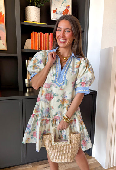 This cream floral dress is basically spring in dress form. With a colorful mix of green, yellow, pink, and blue, it’s bright, cheerful, and made for everything from brunch dates to baby showers. The puff sleeves give it that extra wow factor, while the light blue accent trim along the front, collar, and sleeve cuffs adds the prettiest pop. And don’t even get us started on the neutral scalloped detail—it’s the kind of little touch that makes this dress feel extra special. 