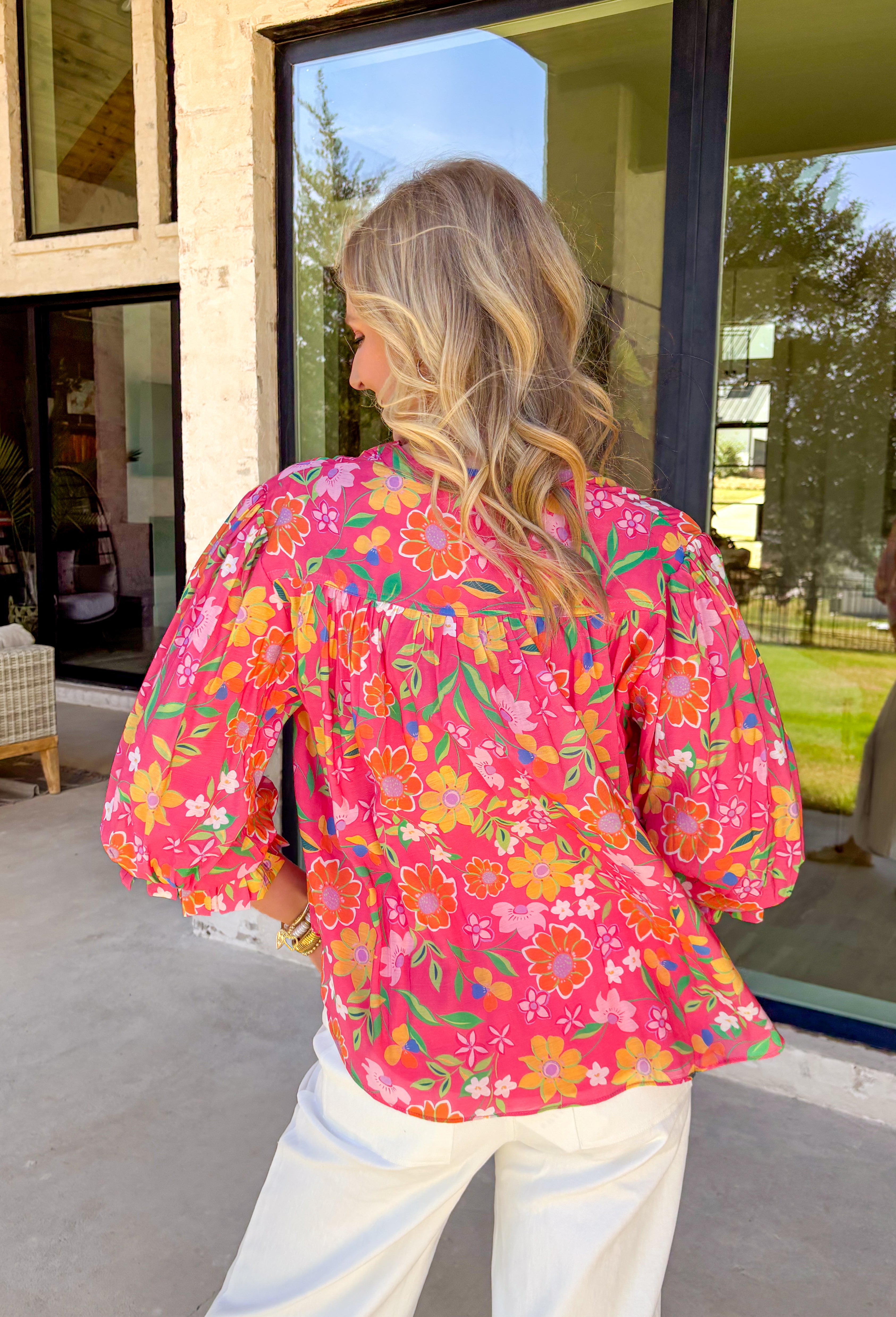 This pink long sleeve top is giving fresh-picked flower energy in the prettiest way. Featuring a colorful floral print in shades of green, yellow, orange, and white, it’s the kind of piece that instantly brightens your day (and your outfit). The pink base keeps it sweet, while the vibrant florals make it feel playful and ready for sunshine. Designed with front button details and elastic cuff sleeves, this top blends classic structure with easy comfort. 