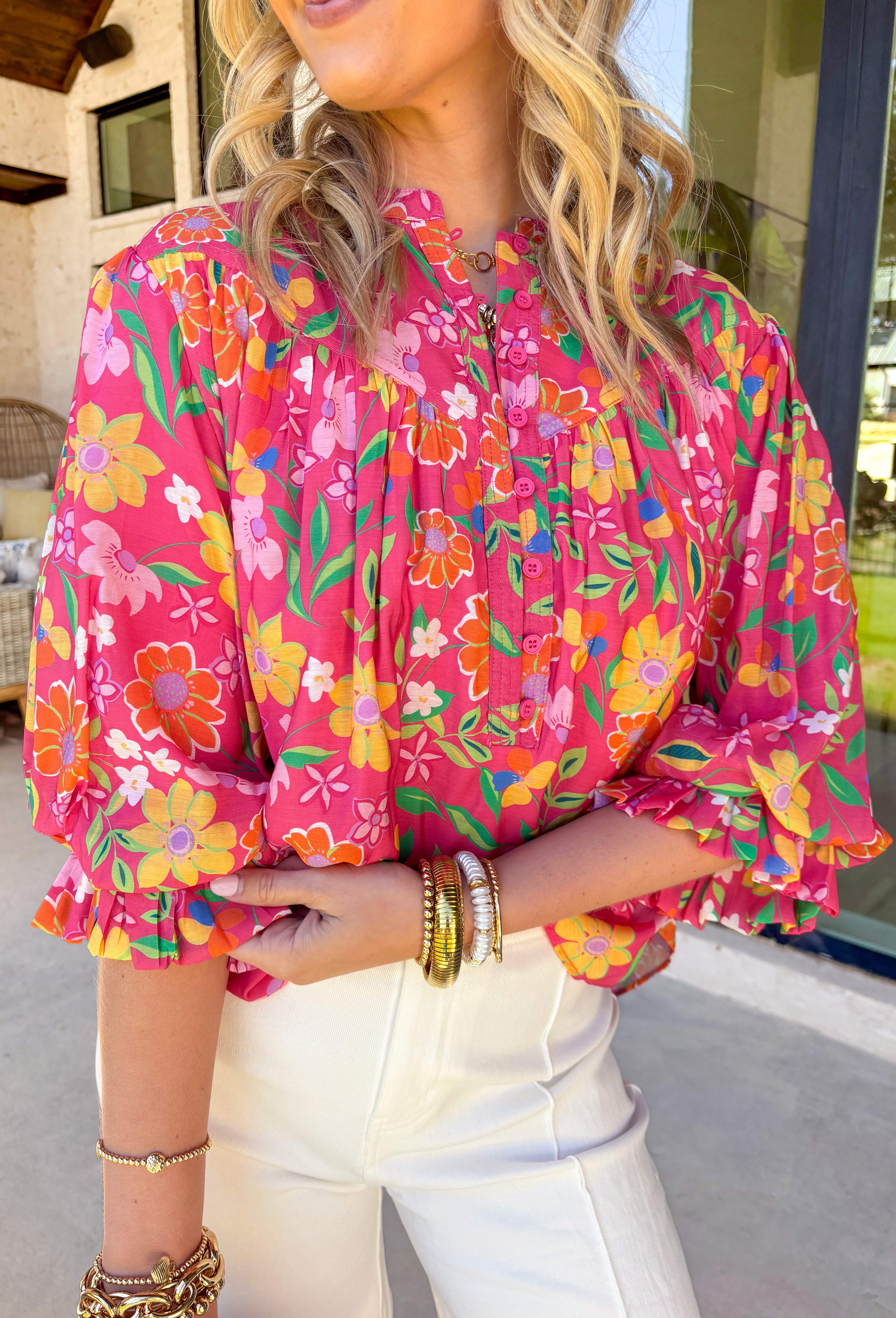 This pink long sleeve top is giving fresh-picked flower energy in the prettiest way. Featuring a colorful floral print in shades of green, yellow, orange, and white, it’s the kind of piece that instantly brightens your day (and your outfit). The pink base keeps it sweet, while the vibrant florals make it feel playful and ready for sunshine. Designed with front button details and elastic cuff sleeves, this top blends classic structure with easy comfort. 