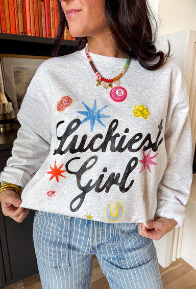 Consider this your official good luck charm! This heathered grey fleece lined sweatshirt features “Luckiest Girl” in bold black lettering, surrounded by the cutest colorful lucky icons — an 8 ball, dice, horseshoe, ladybug, and more. It’s playful, cozy, and full of personality. The soft fleece lining makes it extra comfy for everyday wear, whether you’re running errands, lounging at home, or heading out for a casual day with friends. 
