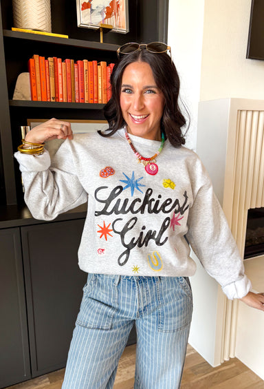 Consider this your official good luck charm! This heathered grey fleece lined sweatshirt features “Luckiest Girl” in bold black lettering, surrounded by the cutest colorful lucky icons — an 8 ball, dice, horseshoe, ladybug, and more. It’s playful, cozy, and full of personality. The soft fleece lining makes it extra comfy for everyday wear, whether you’re running errands, lounging at home, or heading out for a casual day with friends. 