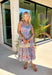 This sleeveless light blue midi dress by Entro is giving major spring picnic energy. With a colorful floral print in pops of red, mustard, and light pink, it’s bright, cheerful, and made for sunny days. The blue and white gingham trim along the top adds the cutest contrast, and the three front tie details bring in that extra sweet, feminine touch we can’t get enough of. 