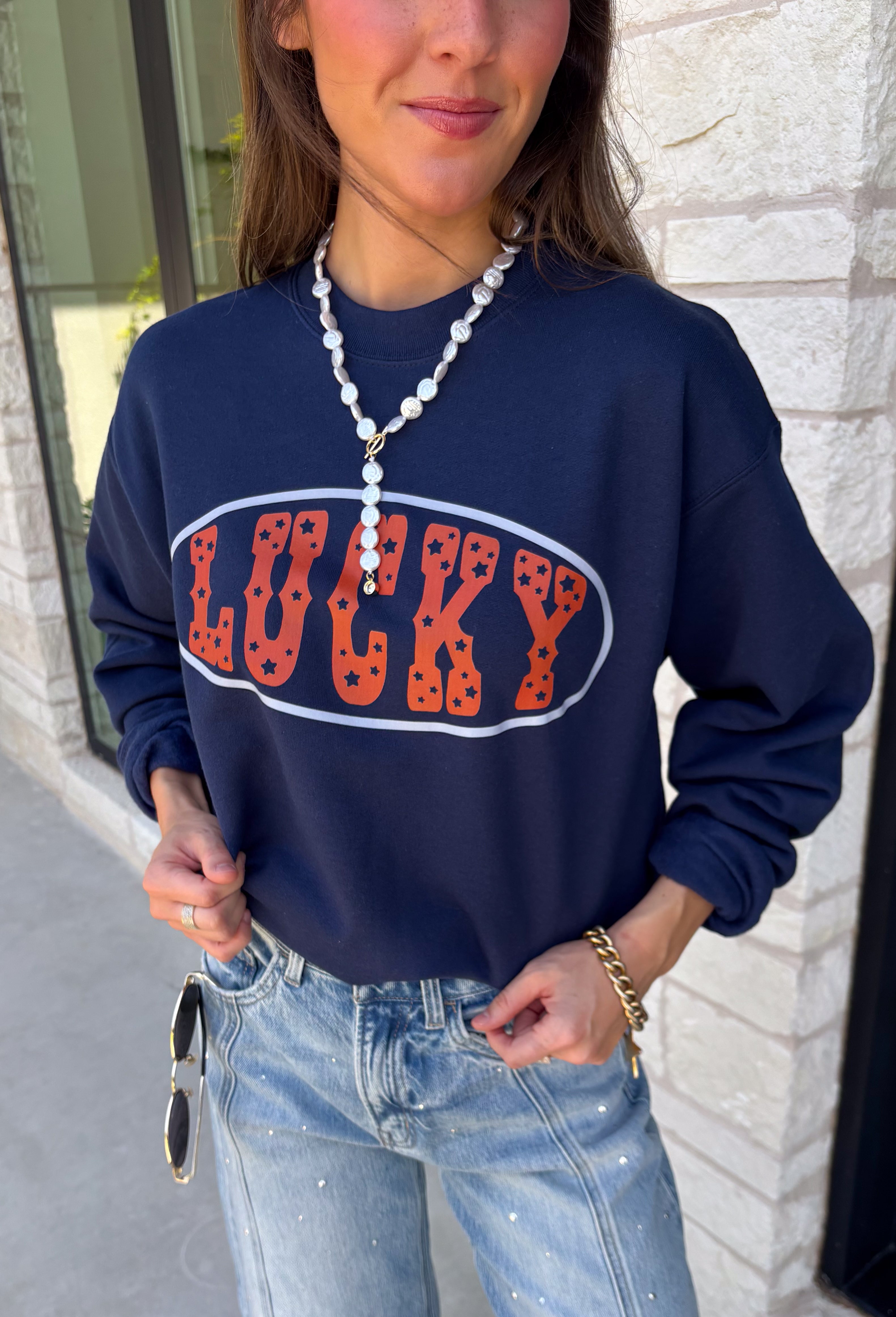 Bring a little extra luck to your cozy season with this playful graphic sweatshirt. Featuring "Lucky" in rust lettering accented with whimsical stars and outlined by a light blue circle, this navy pullover adds the perfect pop of color to your everyday wardrobe. The fleece-lined interior keeps you warm and comfortable, making it the perfect choice for football weekends, coffee runs, casual days, and cozy nights in. It's an easy favorite you'll be reaching for all fall and winter long.