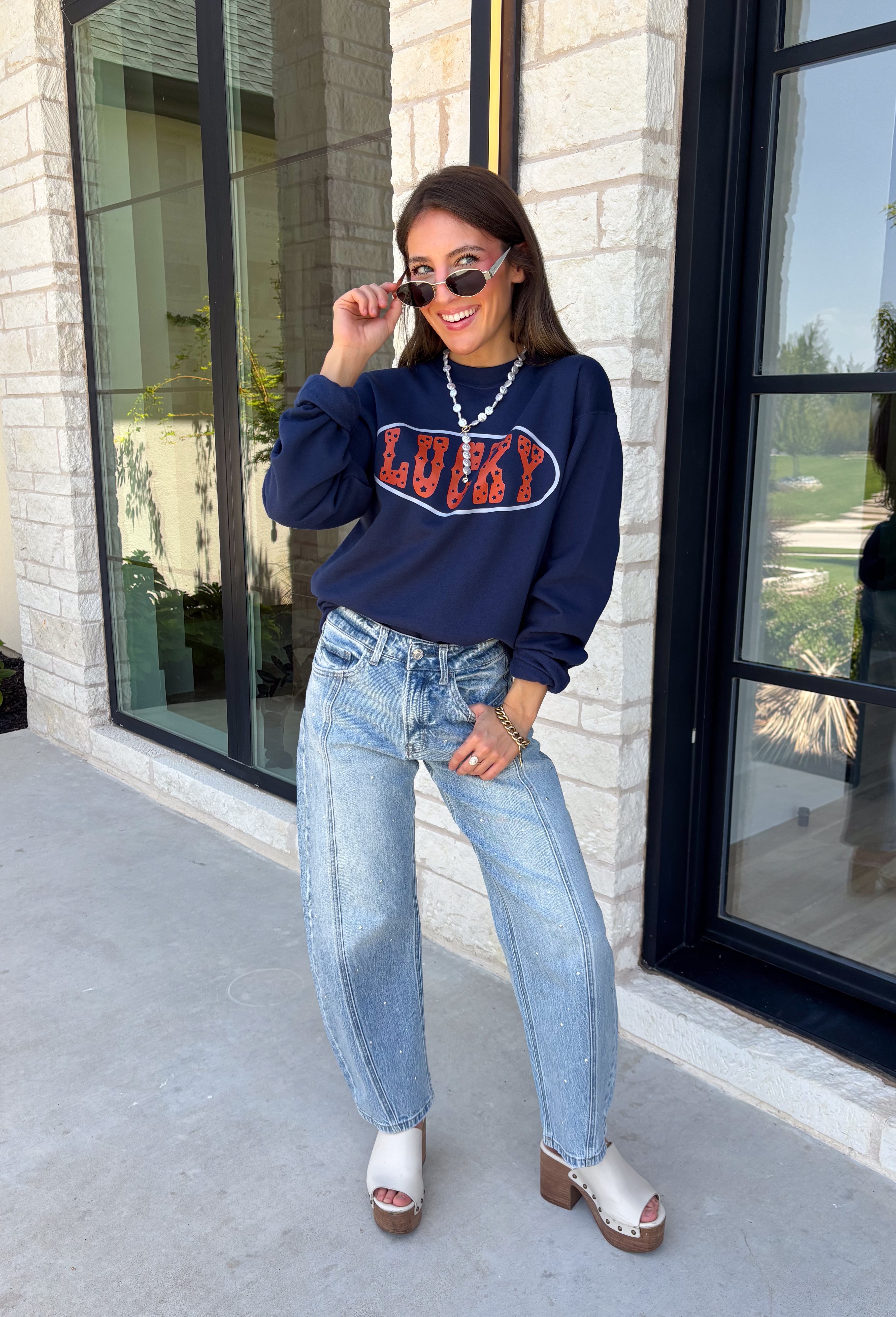 Bring a little extra luck to your cozy season with this playful graphic sweatshirt. Featuring "Lucky" in rust lettering accented with whimsical stars and outlined by a light blue circle, this navy pullover adds the perfect pop of color to your everyday wardrobe. The fleece-lined interior keeps you warm and comfortable, making it the perfect choice for football weekends, coffee runs, casual days, and cozy nights in. It's an easy favorite you'll be reaching for all fall and winter long.