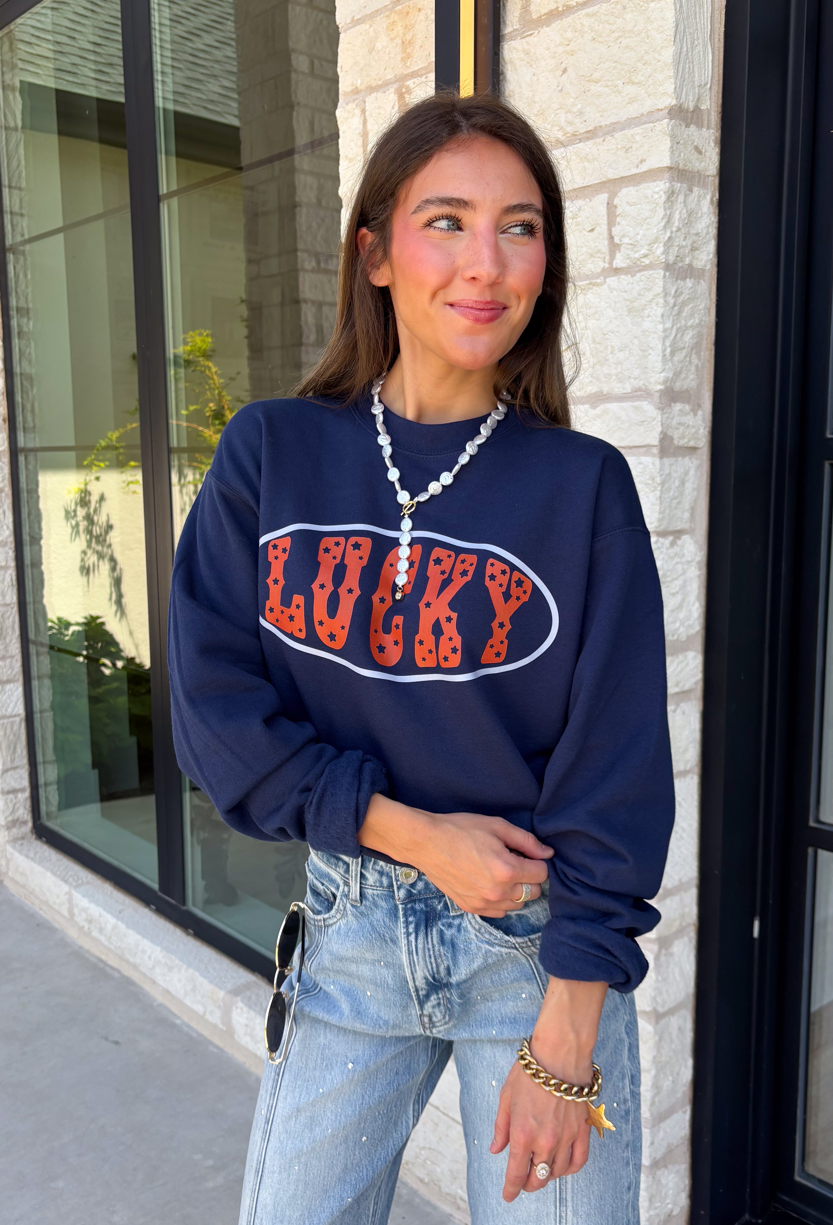 Bring a little extra luck to your cozy season with this playful graphic sweatshirt. Featuring "Lucky" in rust lettering accented with whimsical stars and outlined by a light blue circle, this navy pullover adds the perfect pop of color to your everyday wardrobe. The fleece-lined interior keeps you warm and comfortable, making it the perfect choice for football weekends, coffee runs, casual days, and cozy nights in. It's an easy favorite you'll be reaching for all fall and winter long.