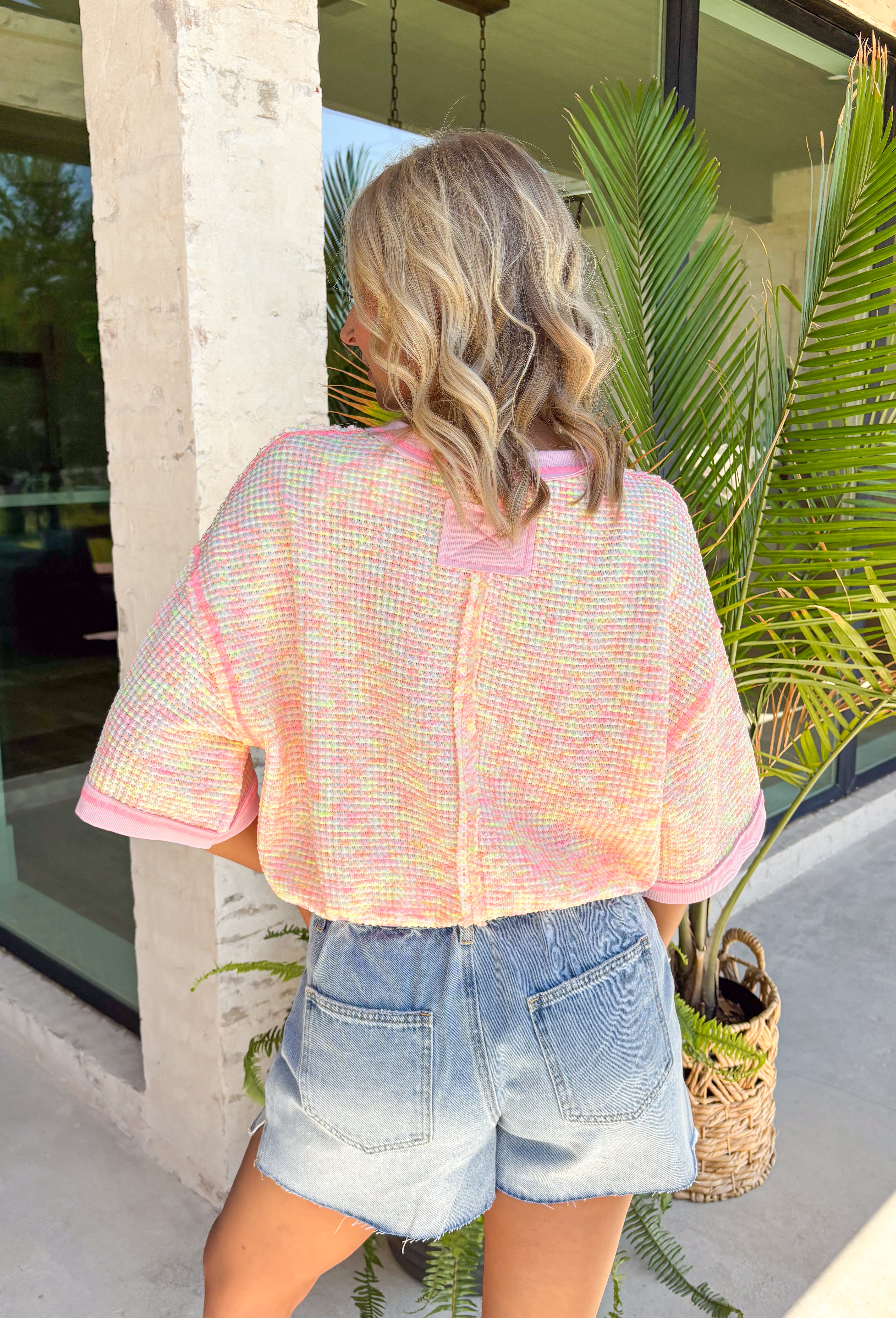 This colorful textured top is the kind of easy, throw-on piece that makes summer dressing fun! With a mix of pink, white, and yellow, it brings a pop of color that feels bright but still easy to style. The waffle texture adds dimension, while the pink trim along the neckline, sleeves, and hem gives it that extra standout detail. Finished with a front pocket for a casual touch, this top is perfect for everyday wear—from errands to coffee runs. Pair it with denim shorts or white jeans and you’re set. 