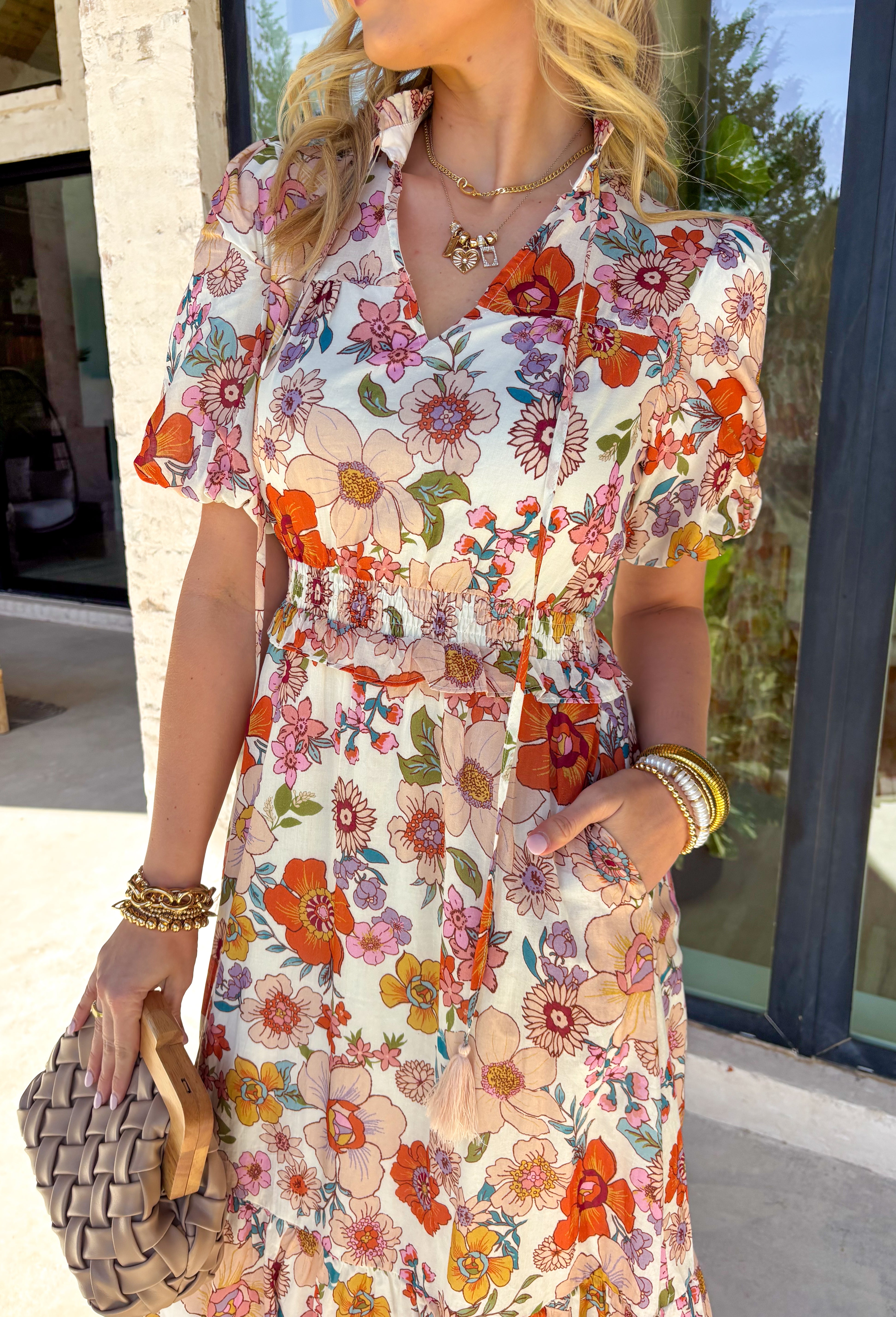 This off white midi dress is bursting with spring color thanks to its vibrant floral print in shades of rust, purple, blue, pink, and brown. The soft cotton fabric keeps it light and breathable, while the flowy midi length makes it perfect for everything from weekend brunch to outdoor showers and special occasions. Designed with feminine puff sleeves and a subtle ruffle neckline, this dress has the sweetest self-tie detail at the top finished with tassels for a playful touch. 