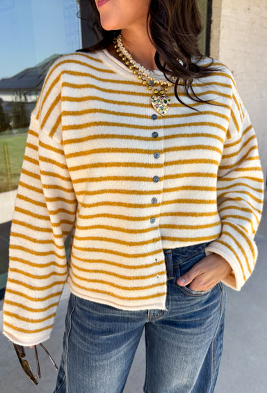 Nothing completes a fall outfit quite like a cozy cardigan. This off white button down cardigan features warm mustard stripes that bring the perfect touch of autumn charm to your wardrobe. The timeless button front makes it easy to wear open or closed, giving you endless styling possibilities throughout the season. Whether you're heading to the office, enjoying a coffee date, or spending the weekend at the pumpkin patch, this soft knit cardigan is one you'll be reaching for again and again.
