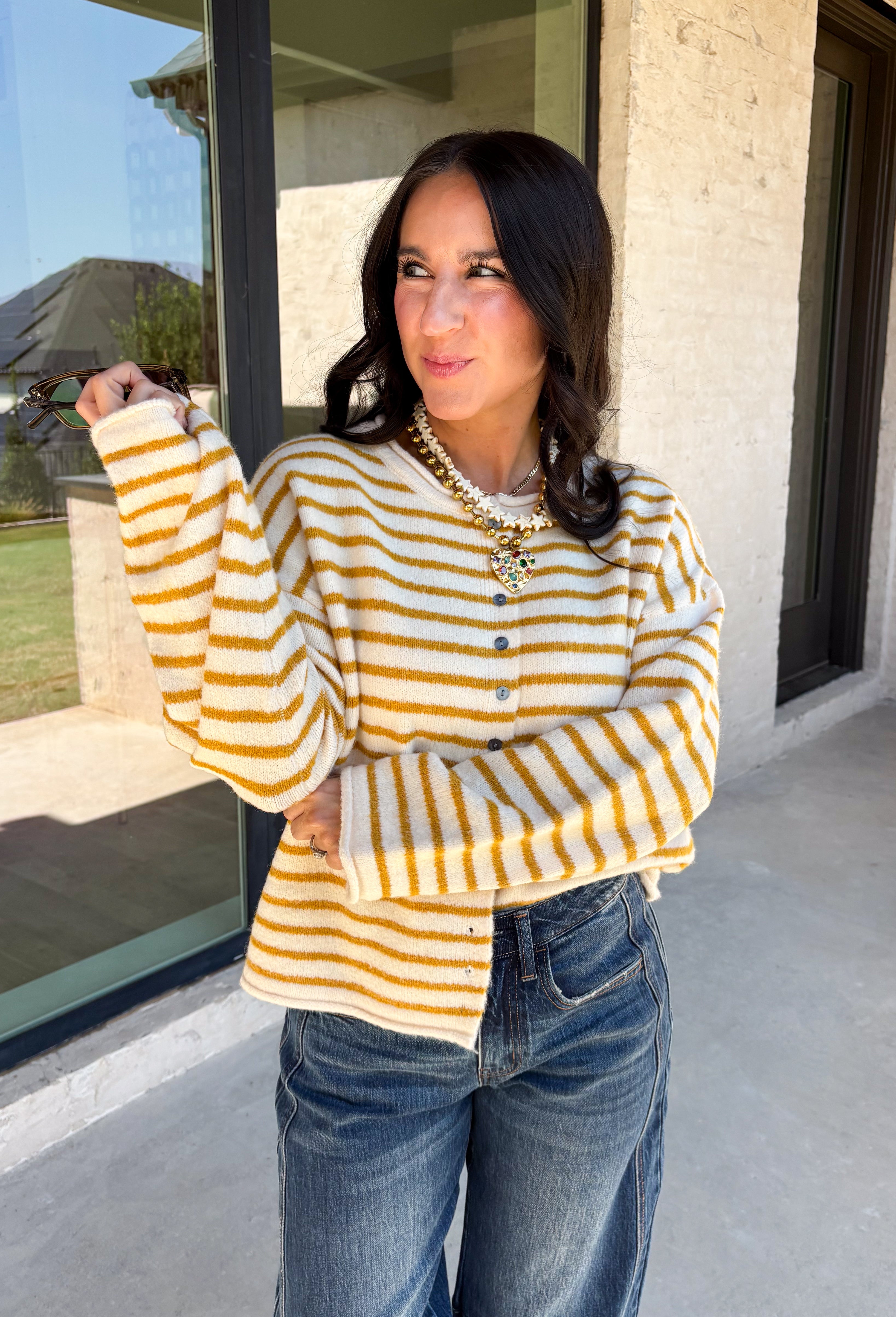 Nothing completes a fall outfit quite like a cozy cardigan. This off white button down cardigan features warm mustard stripes that bring the perfect touch of autumn charm to your wardrobe. The timeless button front makes it easy to wear open or closed, giving you endless styling possibilities throughout the season. Whether you're heading to the office, enjoying a coffee date, or spending the weekend at the pumpkin patch, this soft knit cardigan is one you'll be reaching for again and again.
