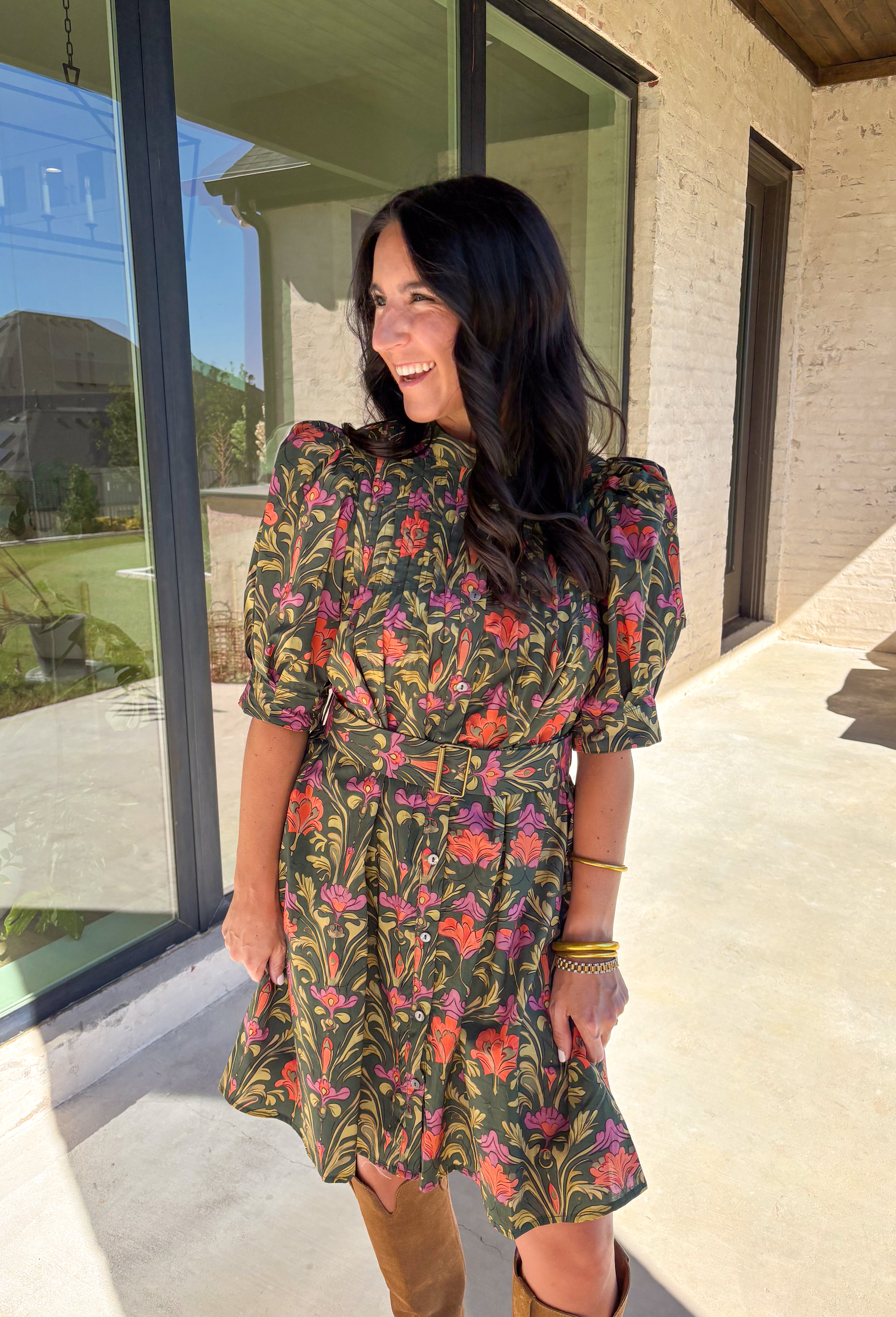 This dark green dress by Entro is a fall favorite with its vibrant botanical print and timeless silhouette. Featuring puff sleeves and pintuck detailing at the front, it brings just the right amount of texture and charm. The matching buckle belt adds shape at the waist, while the button-front closure and side pockets make it as functional as it is flattering. Designed in olive, orange, and pink tones, it’s the perfect balance of classic and playful—made for everything from brunch to fall festivals.
