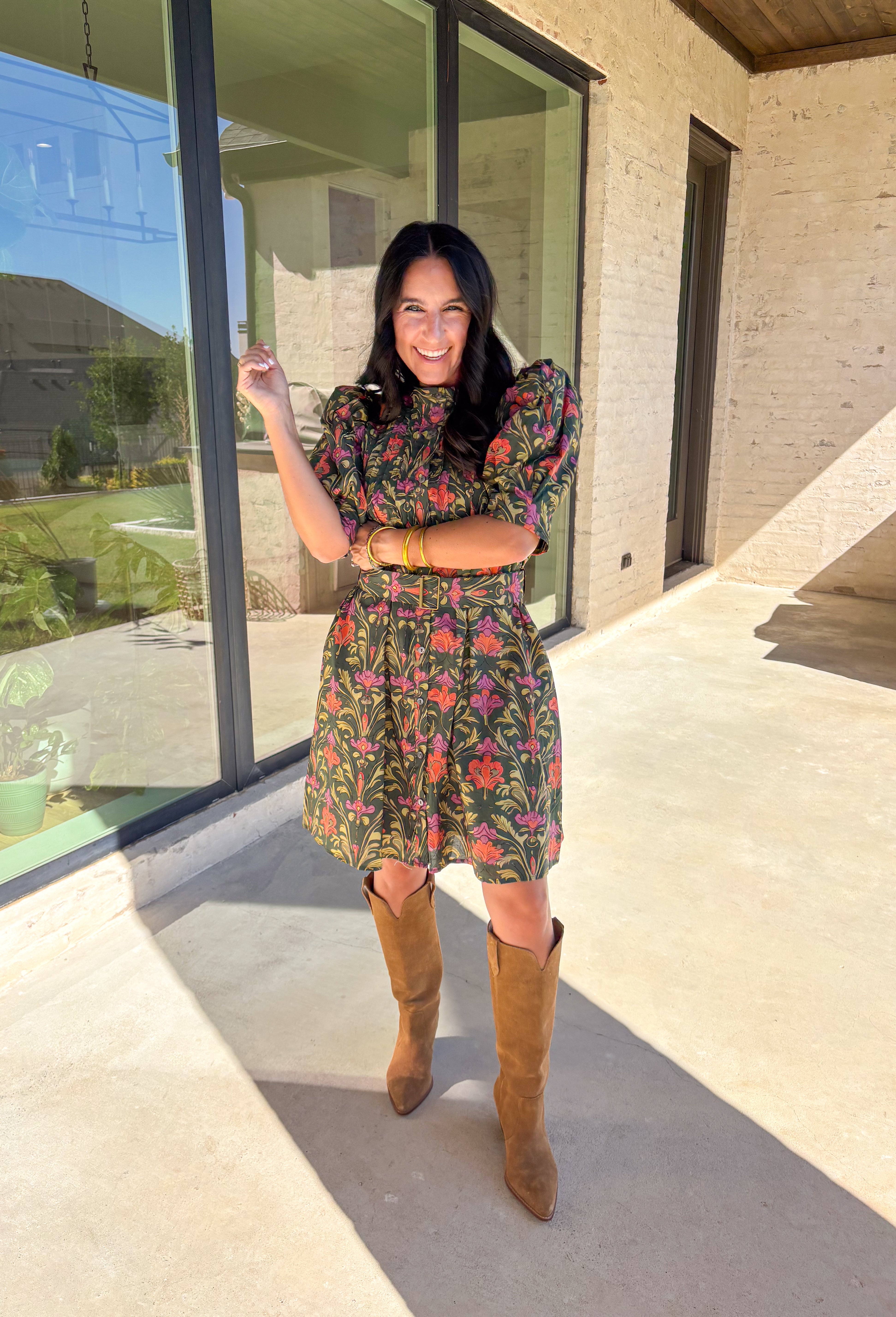 This dark green dress by Entro is a fall favorite with its vibrant botanical print and timeless silhouette. Featuring puff sleeves and pintuck detailing at the front, it brings just the right amount of texture and charm. The matching buckle belt adds shape at the waist, while the button-front closure and side pockets make it as functional as it is flattering. Designed in olive, orange, and pink tones, it’s the perfect balance of classic and playful—made for everything from brunch to fall festivals.