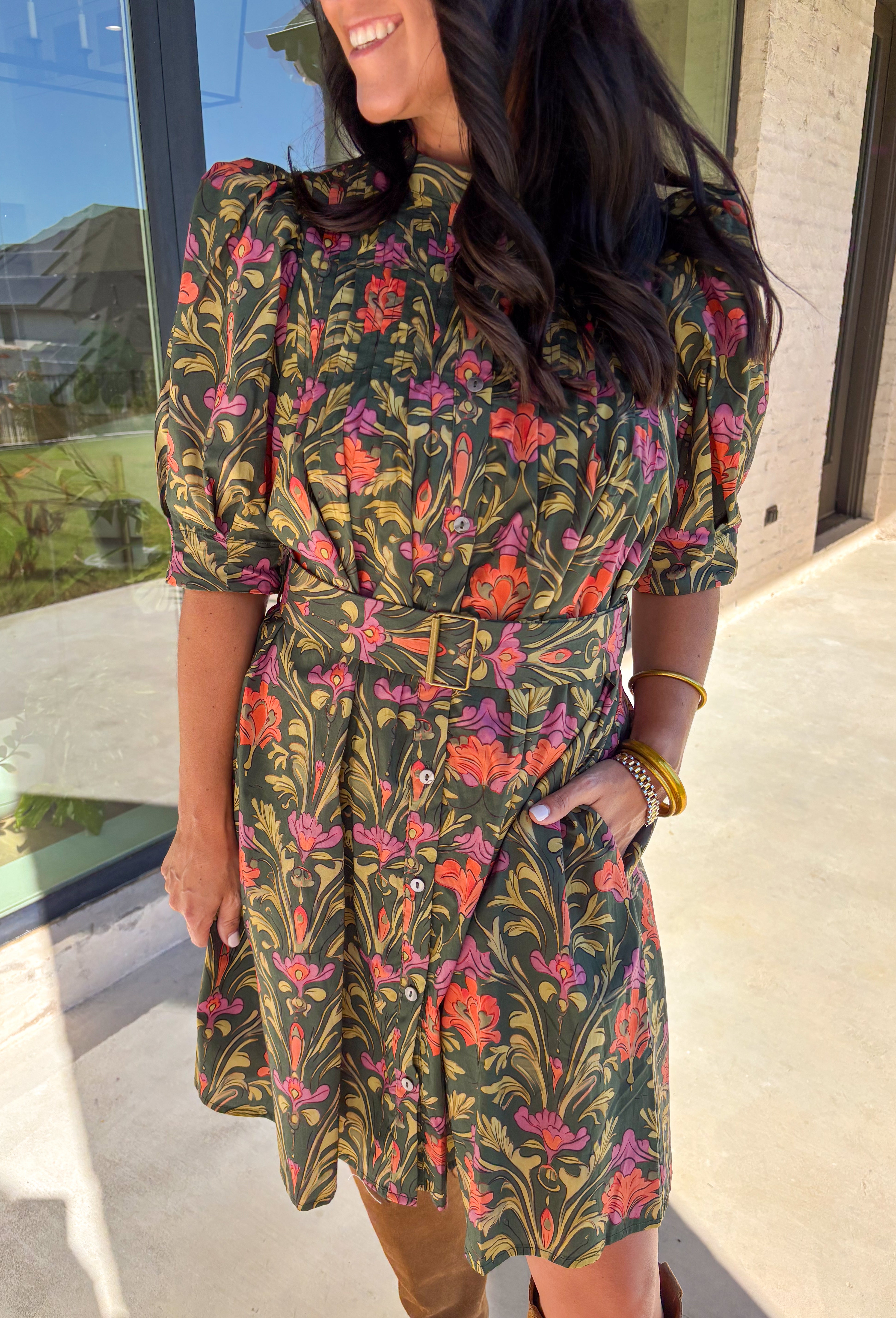 This dark green dress by Entro is a fall favorite with its vibrant botanical print and timeless silhouette. Featuring puff sleeves and pintuck detailing at the front, it brings just the right amount of texture and charm. The matching buckle belt adds shape at the waist, while the button-front closure and side pockets make it as functional as it is flattering. Designed in olive, orange, and pink tones, it’s the perfect balance of classic and playful—made for everything from brunch to fall festivals.