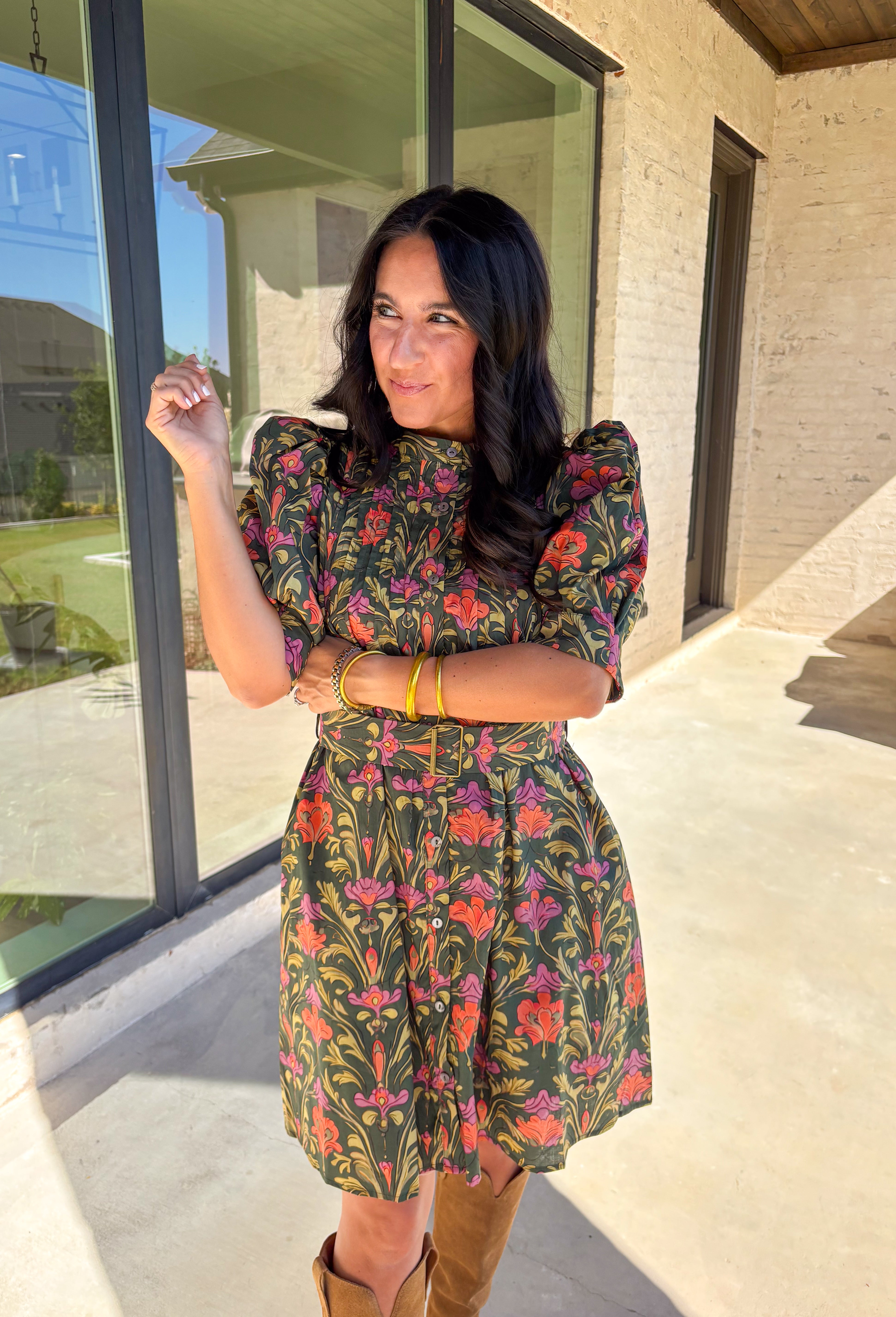 This dark green dress by Entro is a fall favorite with its vibrant botanical print and timeless silhouette. Featuring puff sleeves and pintuck detailing at the front, it brings just the right amount of texture and charm. The matching buckle belt adds shape at the waist, while the button-front closure and side pockets make it as functional as it is flattering. Designed in olive, orange, and pink tones, it’s the perfect balance of classic and playful—made for everything from brunch to fall festivals.