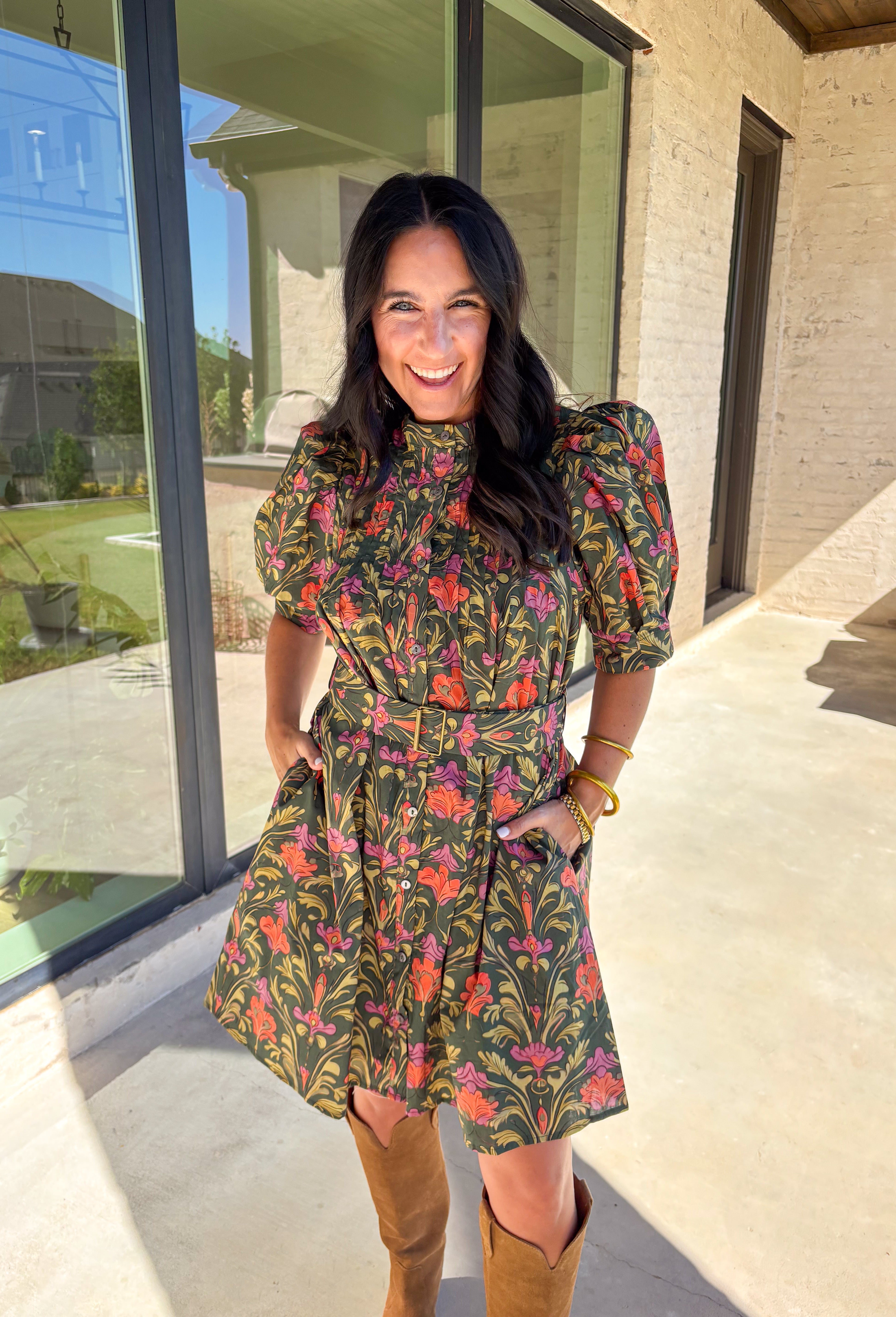 This dark green dress by Entro is a fall favorite with its vibrant botanical print and timeless silhouette. Featuring puff sleeves and pintuck detailing at the front, it brings just the right amount of texture and charm. The matching buckle belt adds shape at the waist, while the button-front closure and side pockets make it as functional as it is flattering. Designed in olive, orange, and pink tones, it’s the perfect balance of classic and playful—made for everything from brunch to fall festivals.