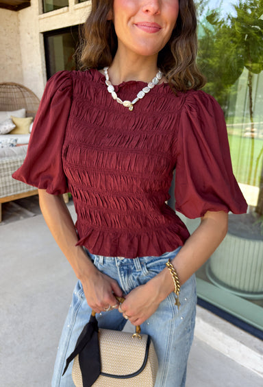 Rich autumn color and feminine details come together beautifully in this brick peplum top. Designed with a flattering smocked bodice, this top offers a comfortable fit while creating a timeless silhouette you'll love. The delicate ruffle neckline and ruffle hem add just the right amount of charm, while the puff sleeves complete the look with a classic fall feel. 