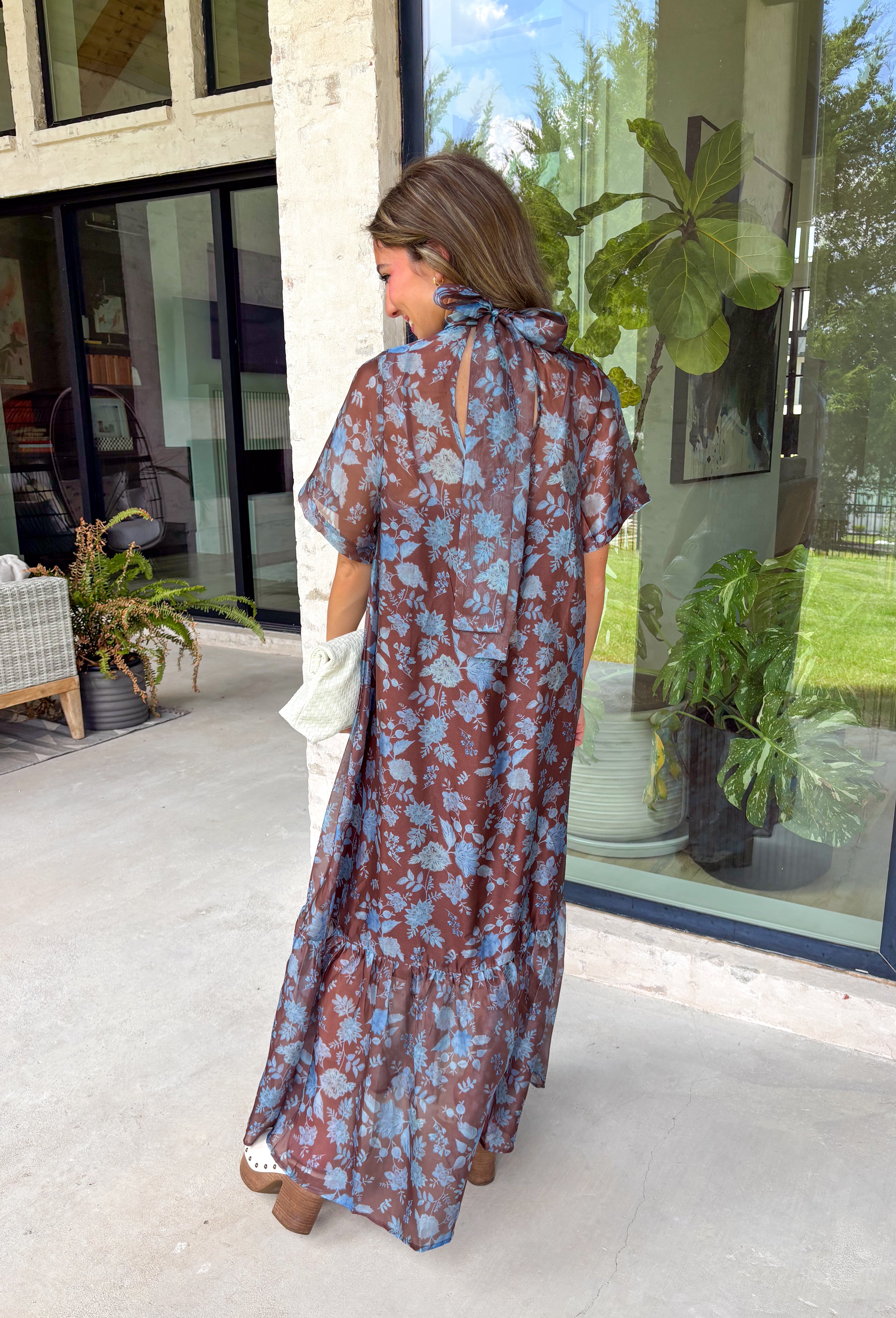 Turn heads at your next special event in this stunning floral maxi dress from Entro. Featuring a rich brown backdrop with a beautiful blue floral print, this elegant dress is designed to make every occasion feel a little more special. The self-tie detail at the back neckline adds a graceful finishing touch, while the flowing maxi silhouette creates effortless movement with every step. 