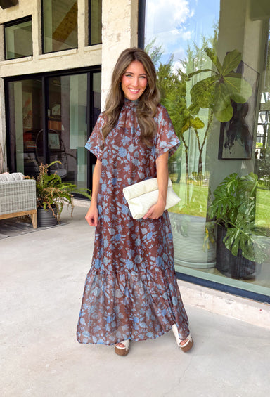 Turn heads at your next special event in this stunning floral maxi dress from Entro. Featuring a rich brown backdrop with a beautiful blue floral print, this elegant dress is designed to make every occasion feel a little more special. The self-tie detail at the back neckline adds a graceful finishing touch, while the flowing maxi silhouette creates effortless movement with every step. 