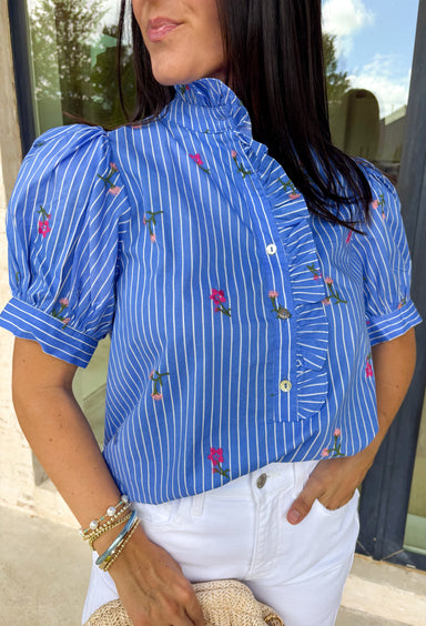 This blue short sleeve top by Entro is giving the perfect mix of classic and cute for spring. Featuring a crisp white stripe print with delicate floral embroidery in green and pink, it’s one of those tops that feels extra special without trying too hard. The button-front design and subtle ruffle detail add a sweet finishing touch, making it easy to dress up with white denim or keep casual with your favorite everyday jeans.