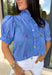 This blue short sleeve top by Entro is giving the perfect mix of classic and cute for spring. Featuring a crisp white stripe print with delicate floral embroidery in green and pink, it’s one of those tops that feels extra special without trying too hard. The button-front design and subtle ruffle detail add a sweet finishing touch, making it easy to dress up with white denim or keep casual with your favorite everyday jeans.