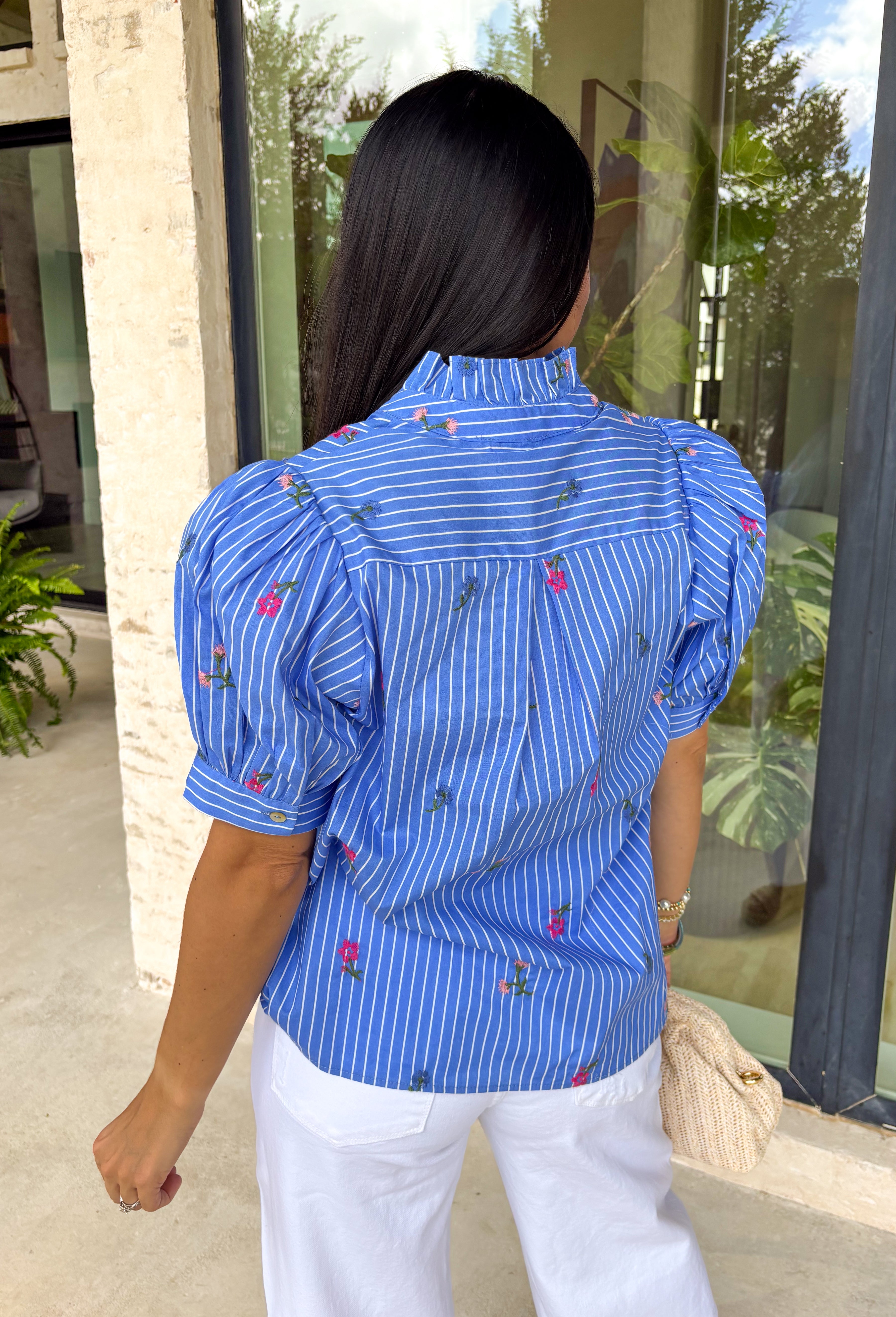 This blue short sleeve top by Entro is giving the perfect mix of classic and cute for spring. Featuring a crisp white stripe print with delicate floral embroidery in green and pink, it’s one of those tops that feels extra special without trying too hard. The button-front design and subtle ruffle detail add a sweet finishing touch, making it easy to dress up with white denim or keep casual with your favorite everyday jeans.