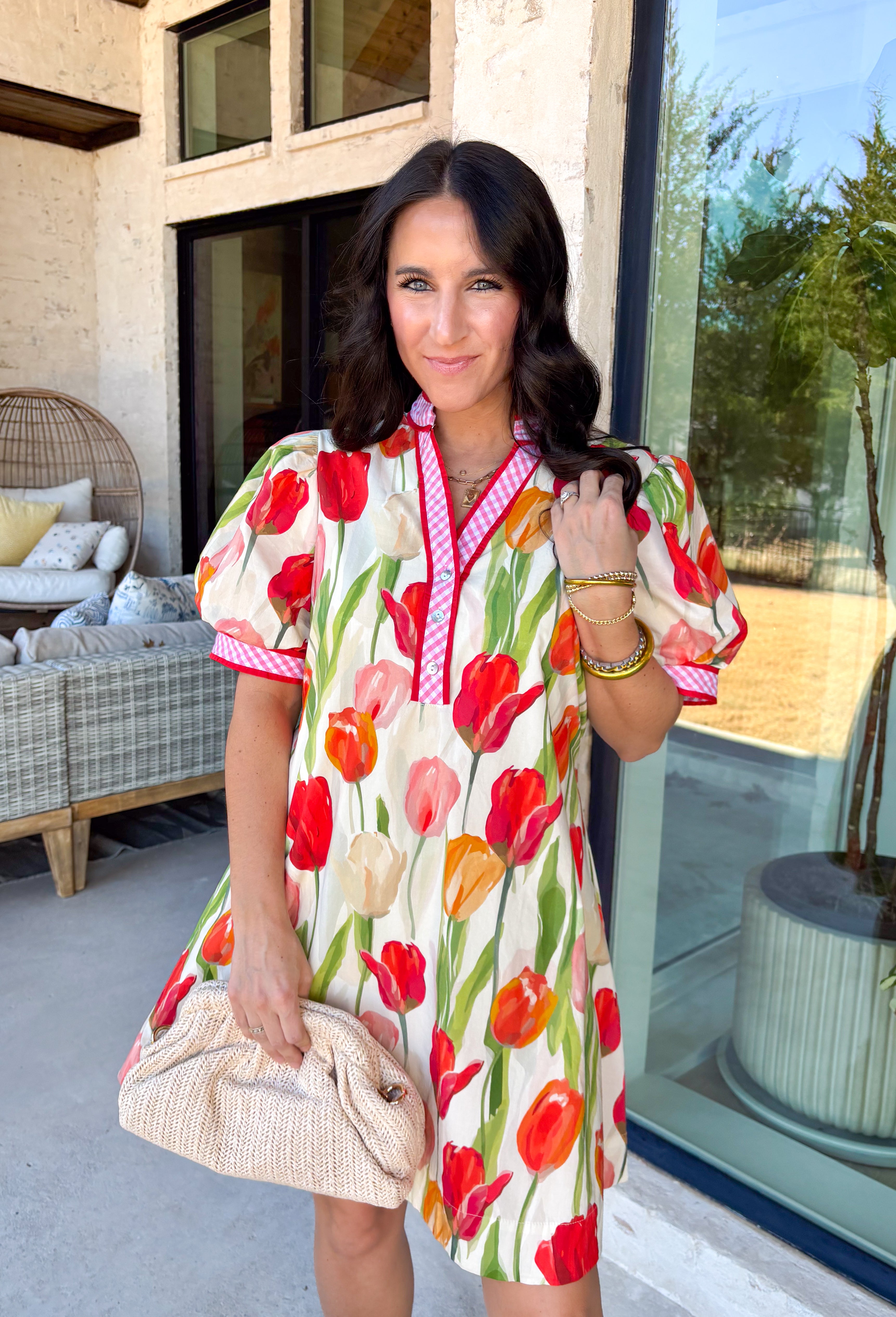 Bold blooms meet playful details in this neutral short sleeve dress that’s made to turn heads this spring. Featuring a vibrant tulip floral print in red, green, orange, and pink, it brings all the happy color while still feeling easy and wearable. The front button detail is accented with red trim and a pink-and-white gingham print for an extra pop of charm. Puff sleeves add a feminine touch, while the adjustable tie detail in the back creates a flattering, customizable fit. 