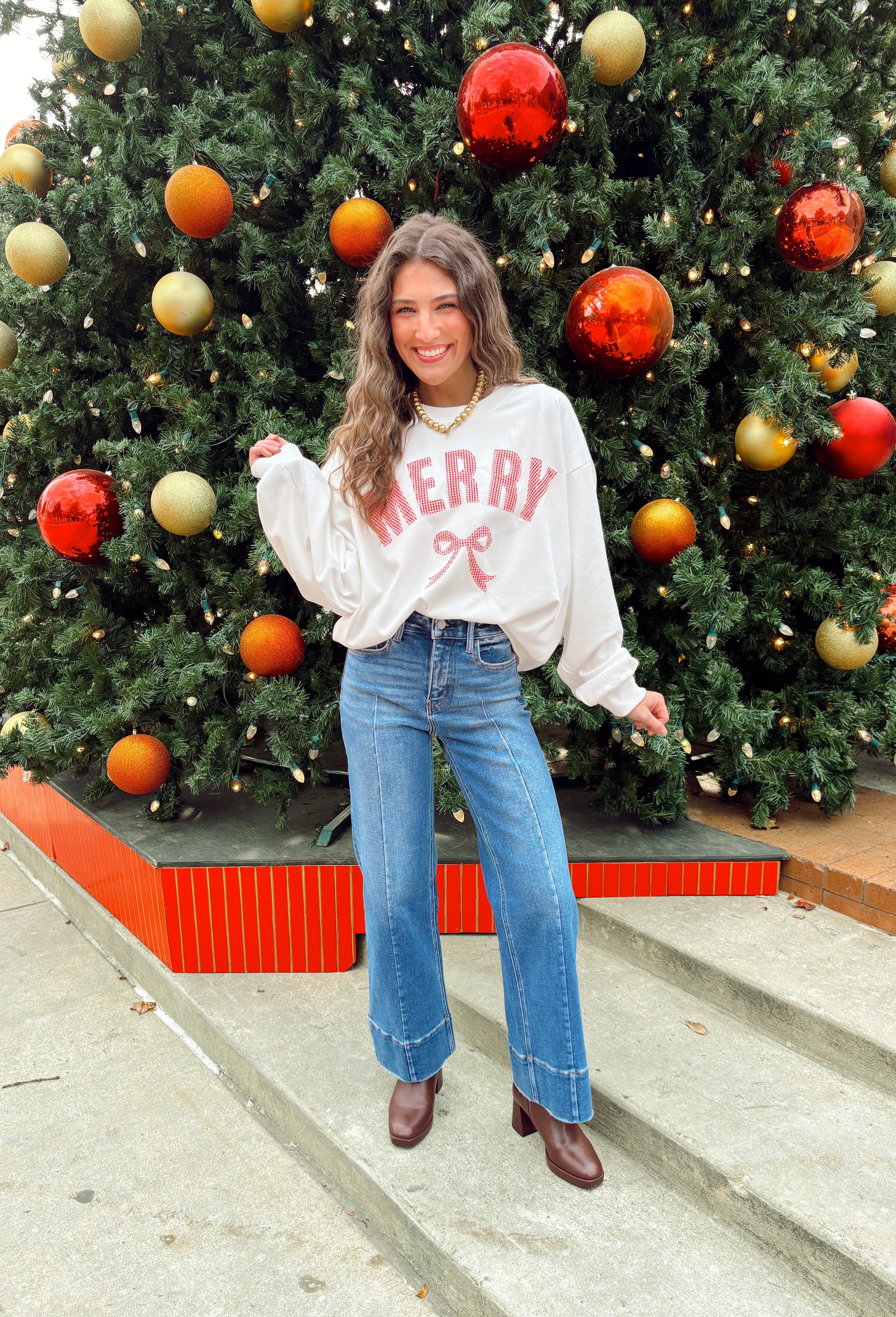 Bring the holiday spirit to life with this adorable “Merry” pullover by Main Strip! Designed in soft white fabric, this lightweight pullover features red and white gingham lettering with delicate white stitching for a festive finish. The matching gingham bow on the front adds the perfect touch of holiday charm. Cozy, comfy, and full of cheer—this pullover is made for everything from Christmas movie marathons to cookie baking days.