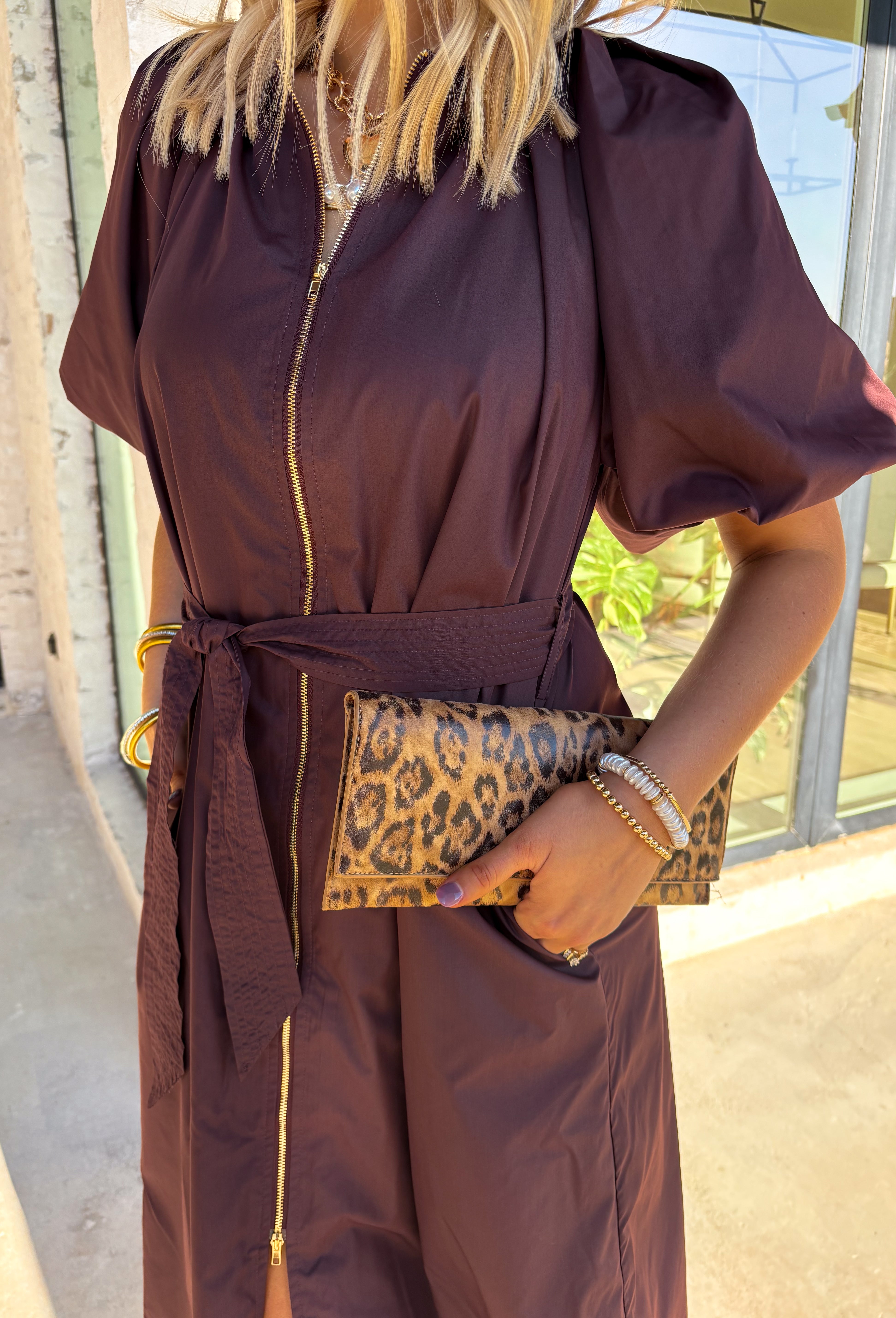 This chocolate brown midi dress by Entro is a flattering mix of modern detail and timeless design. The short puff sleeves and gathered neckline give it a feminine touch, while the exposed front zipper adds a hint of edge. A removable self-tie belt lets you define your waist, and side pockets keep it practical for everyday wear. Fully lined and easy to style, this dress is perfect for transitioning from casual afternoons to evening plans.