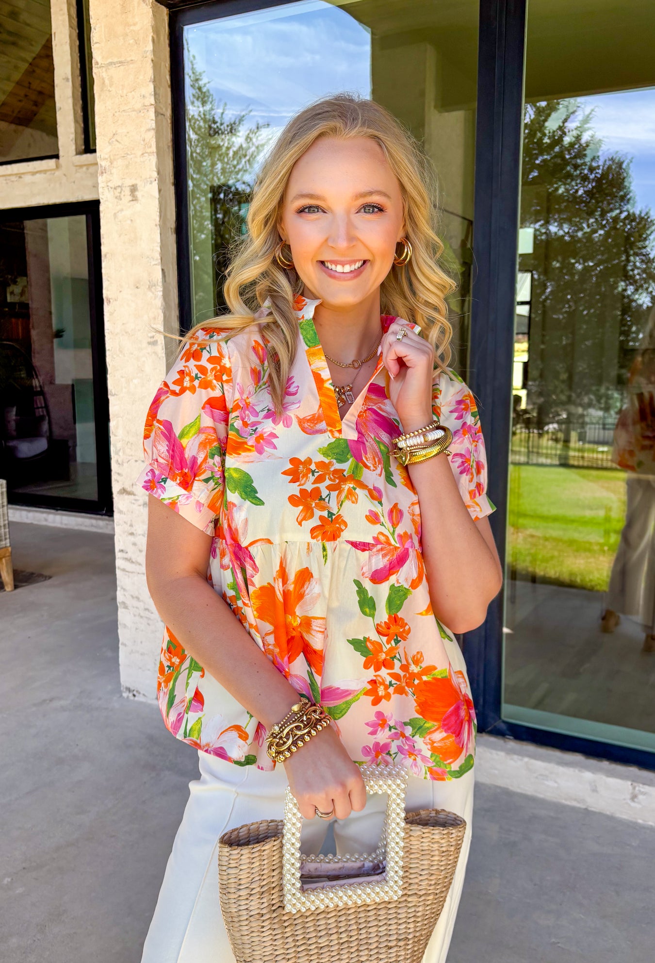 This white babydoll top is giving all the fresh spring energy with its colorful floral print in shades of orange, pink, and green. The relaxed babydoll silhouette flows beautifully, creating that easy, throw-on-and-go fit we all love when the weather starts warming up. It’s light, airy, and made for sunshine-filled days. The flattering v-neckline keeps it feminine and easy to style, while the smocking on the back of the sleeves adds subtle texture and a comfortable fit. 