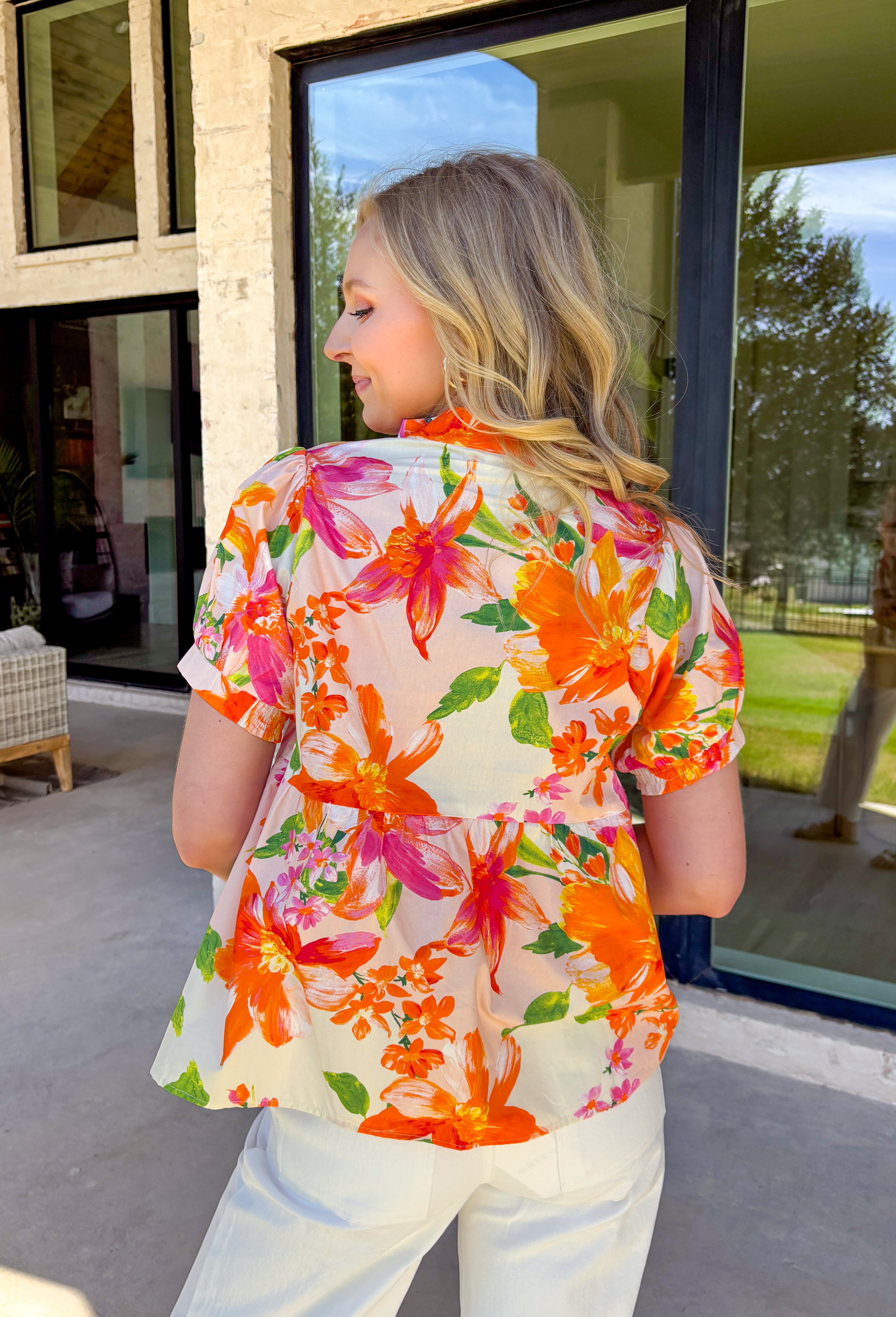 This white babydoll top is giving all the fresh spring energy with its colorful floral print in shades of orange, pink, and green. The relaxed babydoll silhouette flows beautifully, creating that easy, throw-on-and-go fit we all love when the weather starts warming up. It’s light, airy, and made for sunshine-filled days. The flattering v-neckline keeps it feminine and easy to style, while the smocking on the back of the sleeves adds subtle texture and a comfortable fit. 