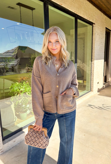Warm, polished, and easy to wear—this brown knit cardigan is the perfect cozy layer for fall. The mock neck keeps the look refined, while hammered gold-tone buttons add a touch of shine to the button-front closure. Front pockets make it as practical as it is stylish, and the soft knit blend with a hint of wool offers just the right amount of warmth for crisp days. Whether layered over a dress or paired with jeans, it’s a seasonal staple you’ll reach for again and again.