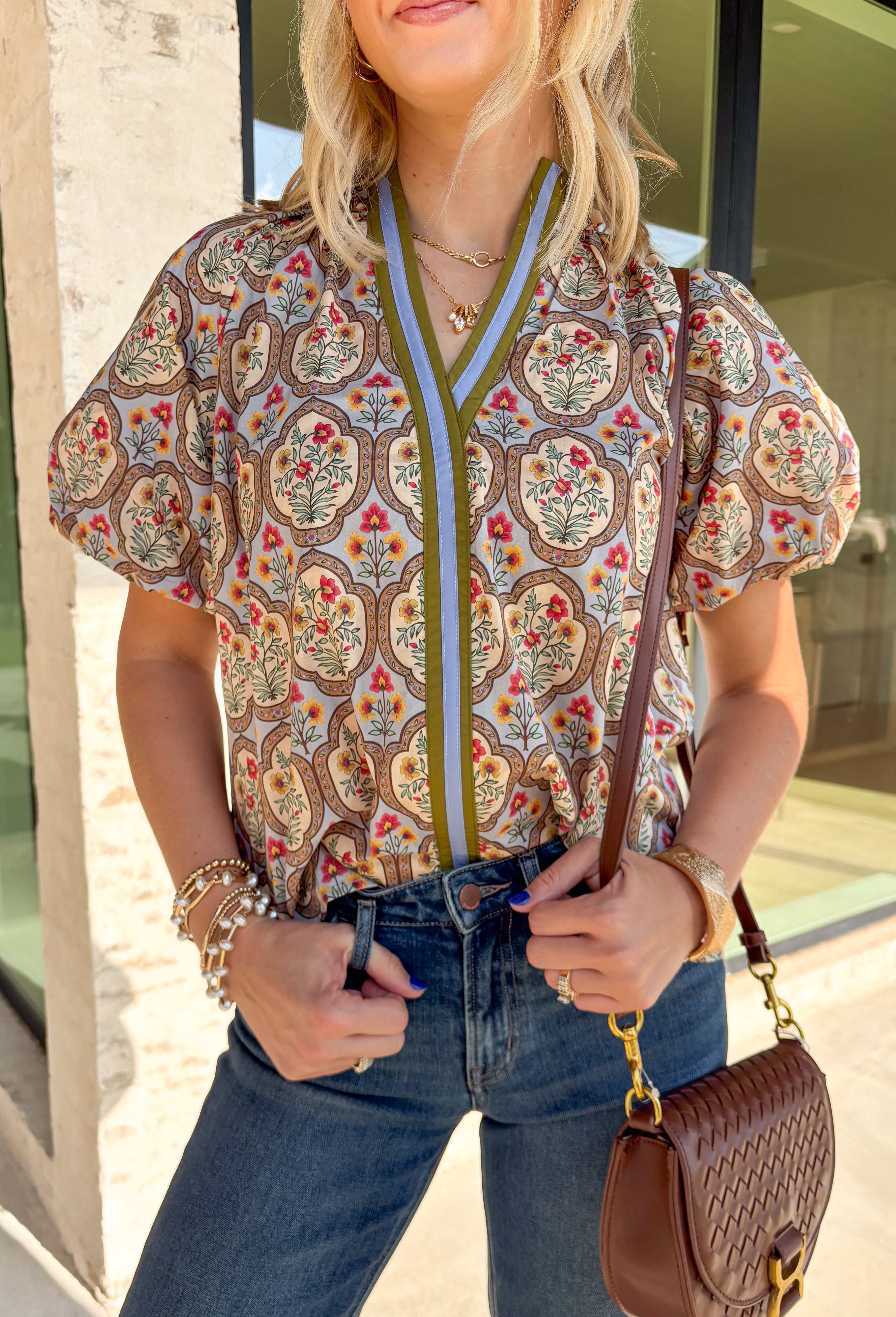 Bring a fresh take on fall florals to your wardrobe with this beautifully detailed top from Entro. Designed with a soft light blue backdrop and a floral print in rich autumn shades, this feminine blouse is full of charming details. Blue and olive contrast trim along the front adds a unique pop of color, while the subtle ruffle neckline and puff sleeves create a timeless, polished silhouette. Crafted from breathable cotton, this versatile top is perfect for everything from workdays to weekend brunches.
