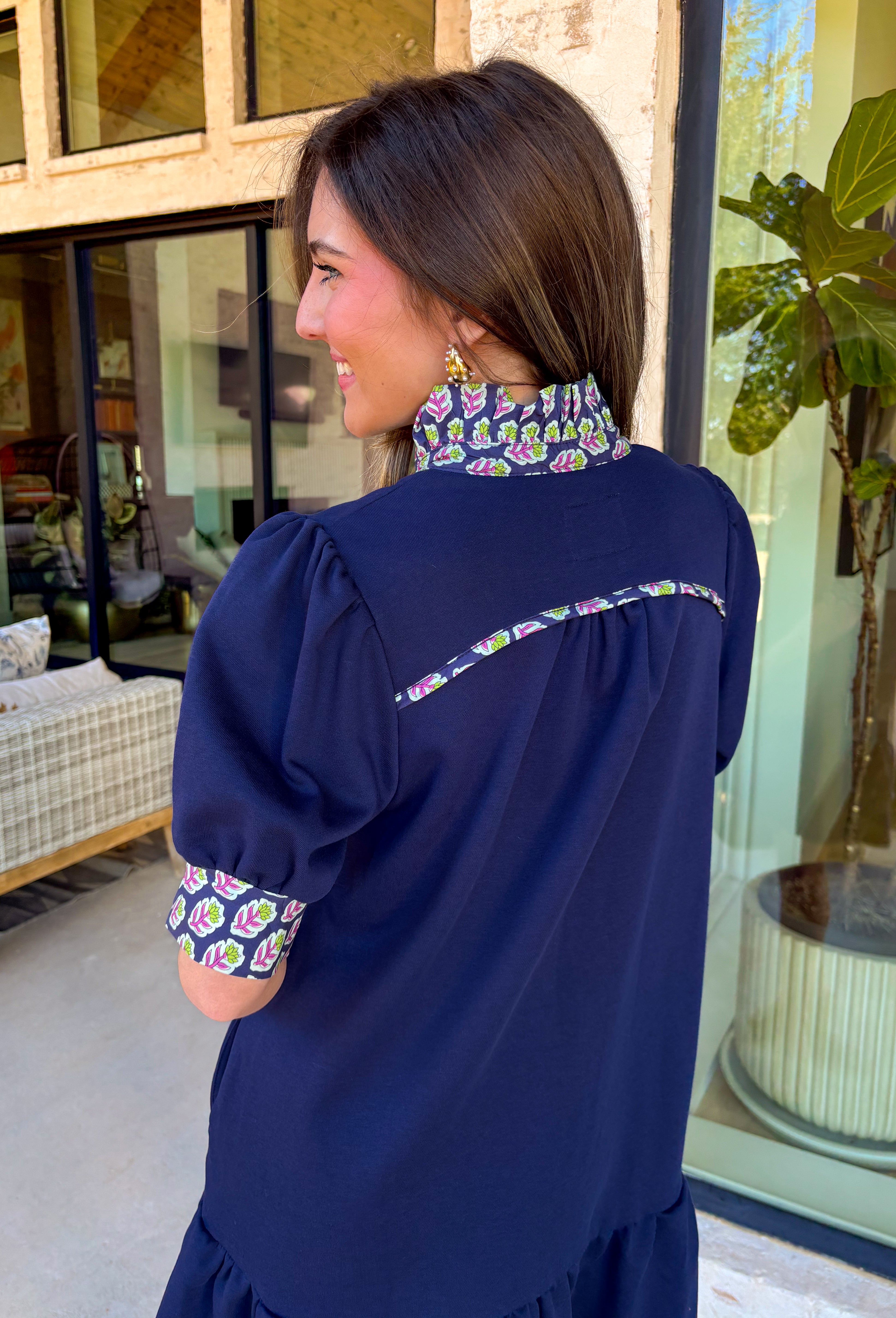 This navy dress is the definition of easy spring style with a little something special! The soft tiered skirt gives it that breezy, swishy movement we love, while the purple and green floral print along the neckline and sleeve cuffs adds the prettiest pop of color. Finished with a single matching button detail on the front (so cute and subtle), plus side pockets for extra everyday ease—this one is made for sunny days, casual plans, and feeling effortlessly put-together.