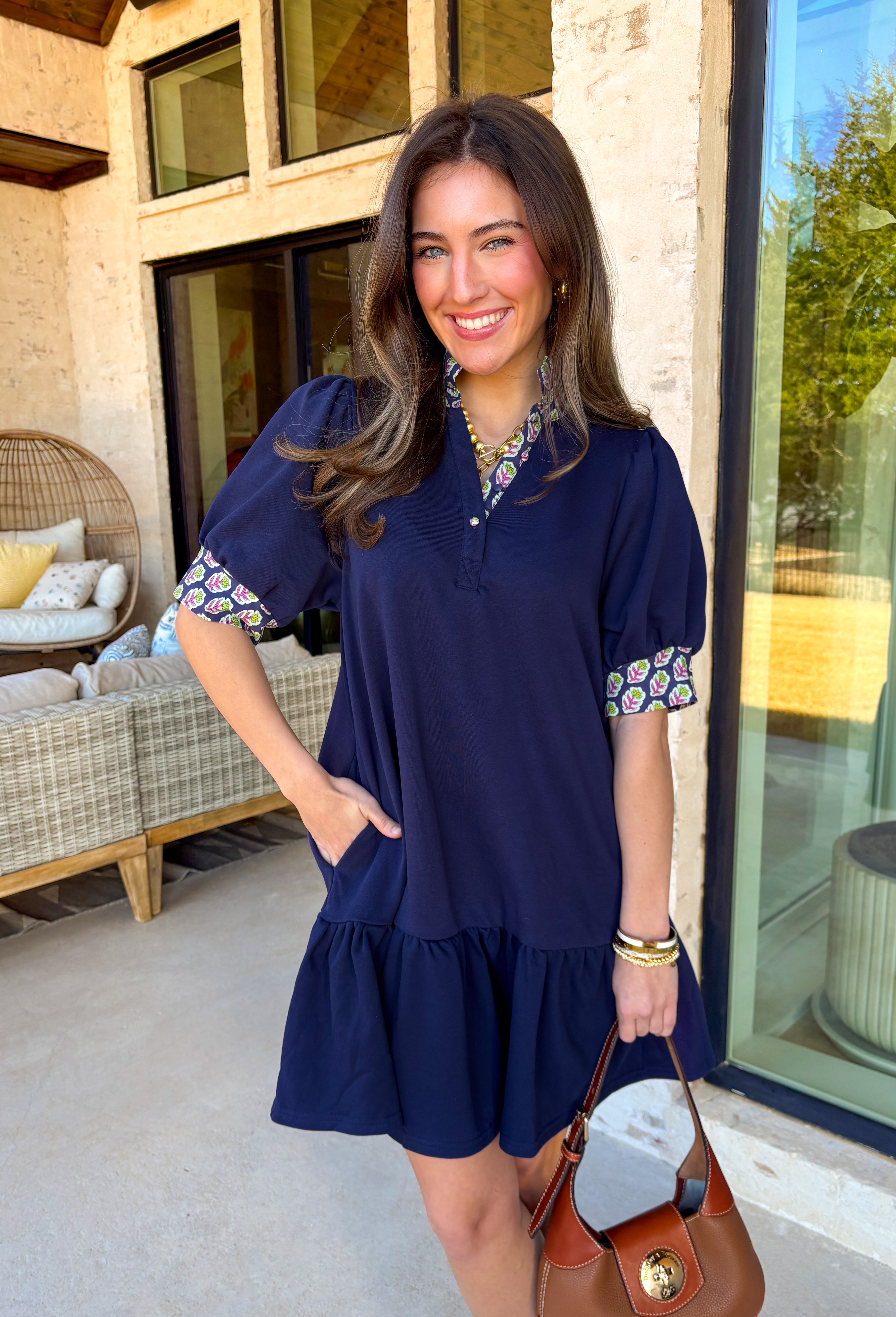 This navy dress is the definition of easy spring style with a little something special! The soft tiered skirt gives it that breezy, swishy movement we love, while the purple and green floral print along the neckline and sleeve cuffs adds the prettiest pop of color. Finished with a single matching button detail on the front (so cute and subtle), plus side pockets for extra everyday ease—this one is made for sunny days, casual plans, and feeling effortlessly put-together.