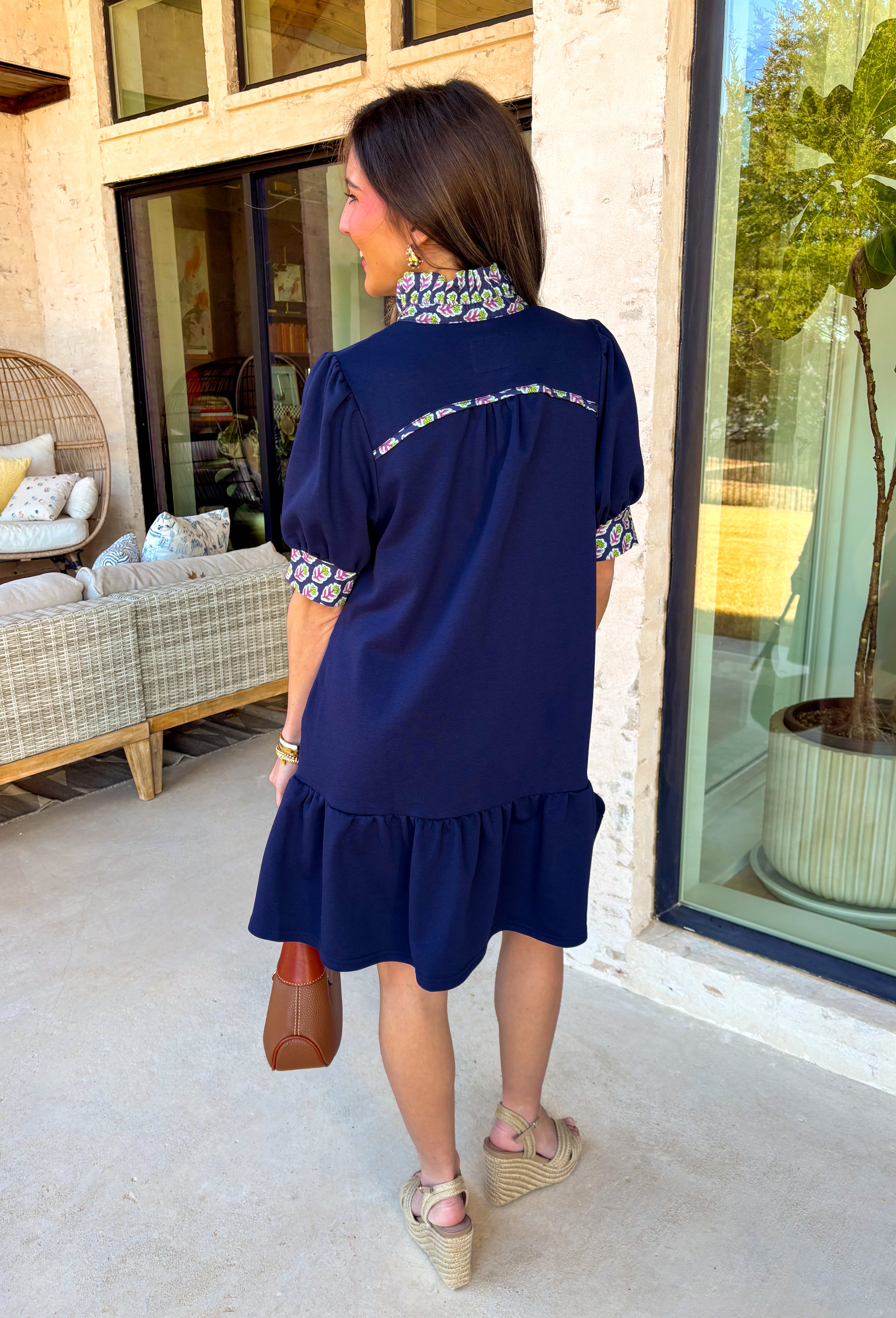This navy dress is the definition of easy spring style with a little something special! The soft tiered skirt gives it that breezy, swishy movement we love, while the purple and green floral print along the neckline and sleeve cuffs adds the prettiest pop of color. Finished with a single matching button detail on the front (so cute and subtle), plus side pockets for extra everyday ease—this one is made for sunny days, casual plans, and feeling effortlessly put-together.
