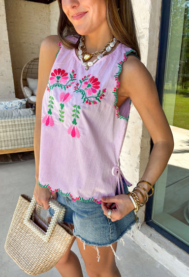 This light pink stripe tank is the sweetest mix of playful and feminine for summer! Featuring pink, red, and green floral embroidery, it adds the prettiest pop of color against the soft striped base. The scalloped hem and sleeves give it that extra delicate detail, while the side tie accents and keyhole back keep it feeling unique and thoughtfully designed. Lightweight and breathable in 100% cotton, it’s perfect for warm days when you want to feel cute and put together. 