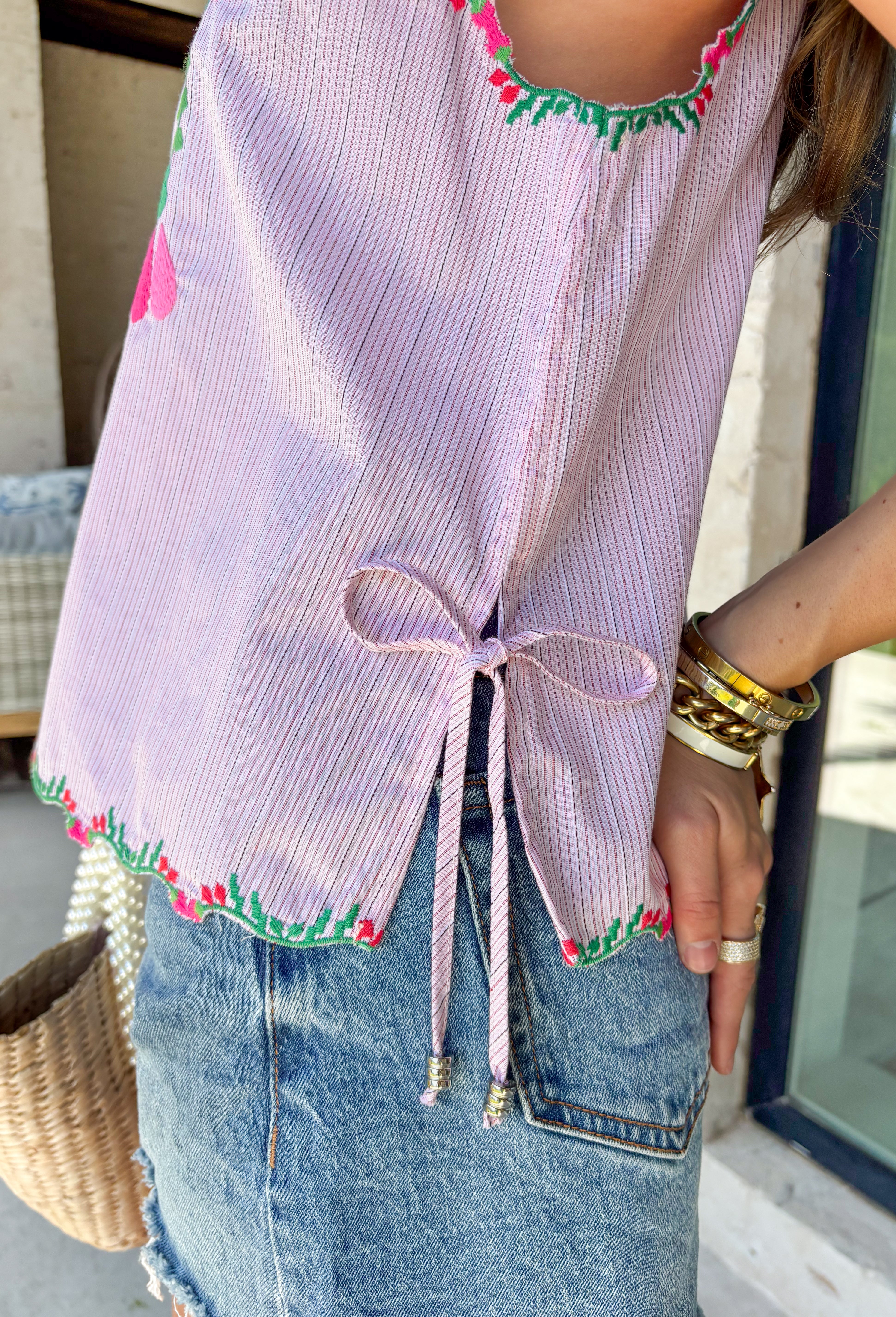 This light pink stripe tank is the sweetest mix of playful and feminine for summer! Featuring pink, red, and green floral embroidery, it adds the prettiest pop of color against the soft striped base. The scalloped hem and sleeves give it that extra delicate detail, while the side tie accents and keyhole back keep it feeling unique and thoughtfully designed. Lightweight and breathable in 100% cotton, it’s perfect for warm days when you want to feel cute and put together. 
