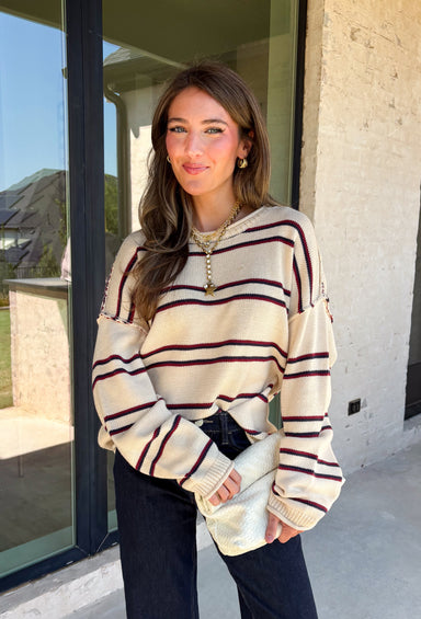 Nothing says cozy season quite like a classic striped sweater! This soft neutral knit is accented with timeless navy and burgundy stripes, creating the perfect color combination for fall. Exposed hems give it a relaxed, lived-in feel, while the ribbed neckline, cuffs, and hem add a polished finish. Whether you're headed to a football game, a weekend getaway, or simply enjoying a crisp autumn day, this cozy sweater is one you'll love reaching for.